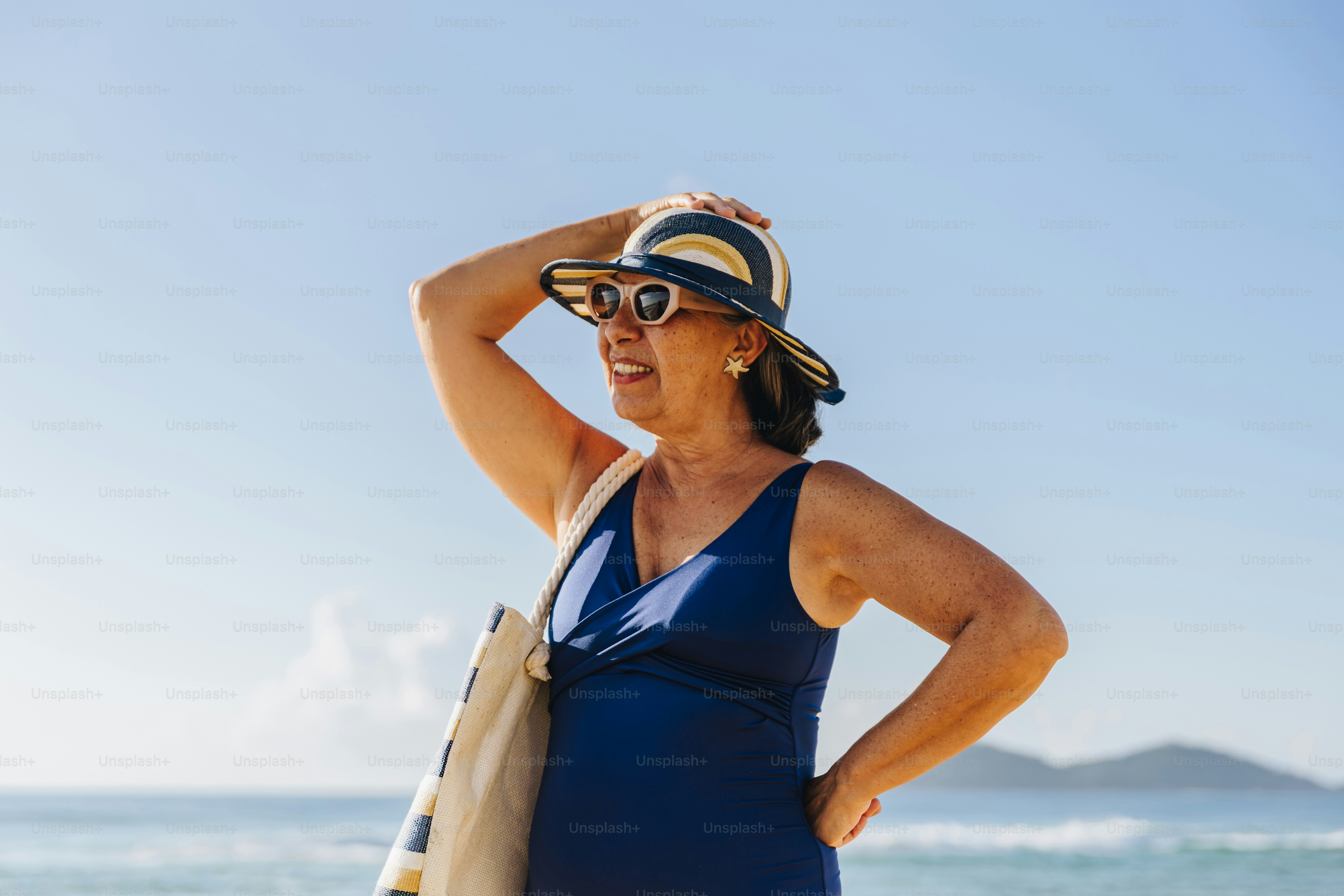 Woman in swimsuit and hat at the beach.