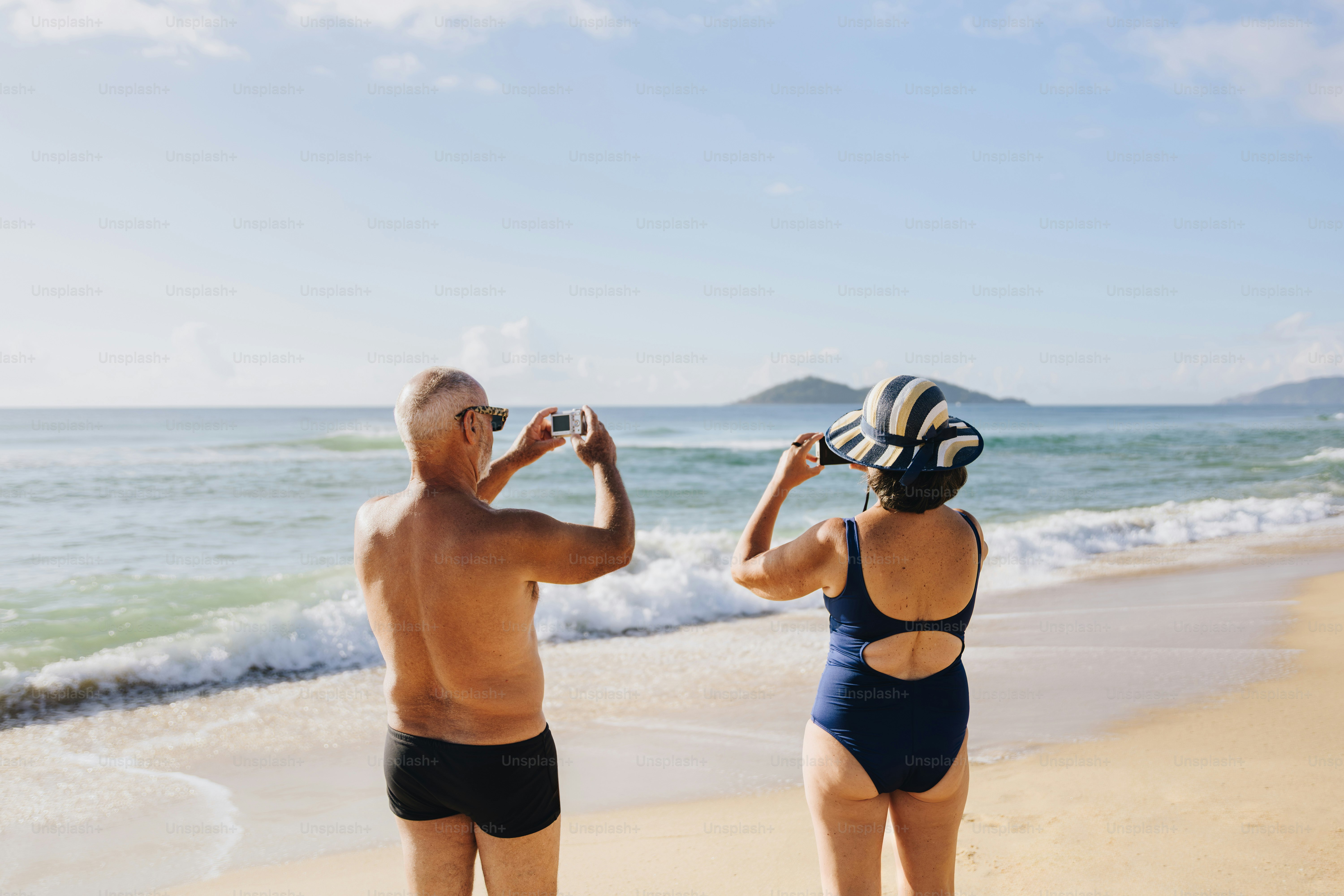 Elderly couple taking photos on a sunny beach.