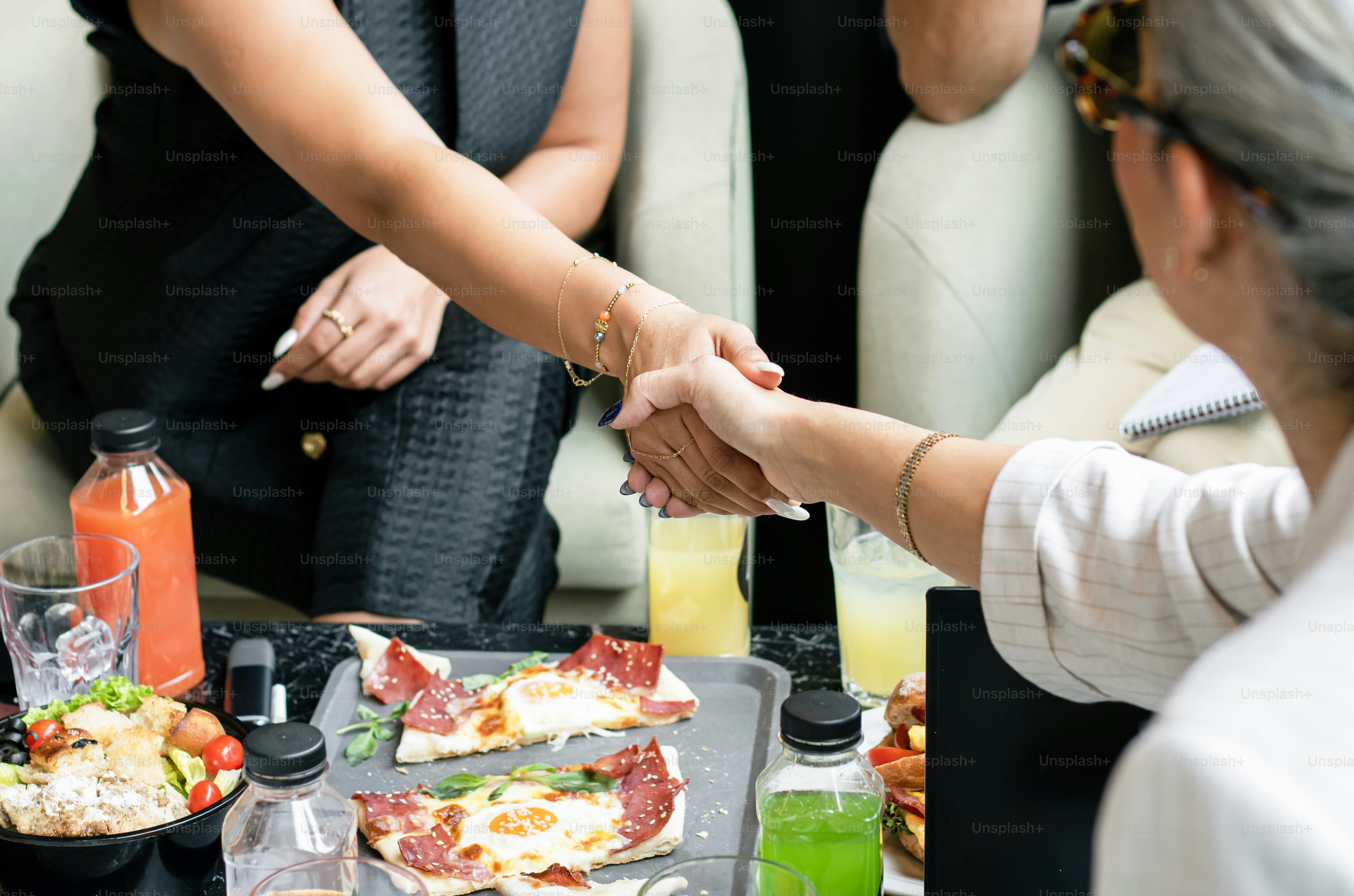 Zwei Frauen schütteln sich über einem Tisch mit Essen die Hand.