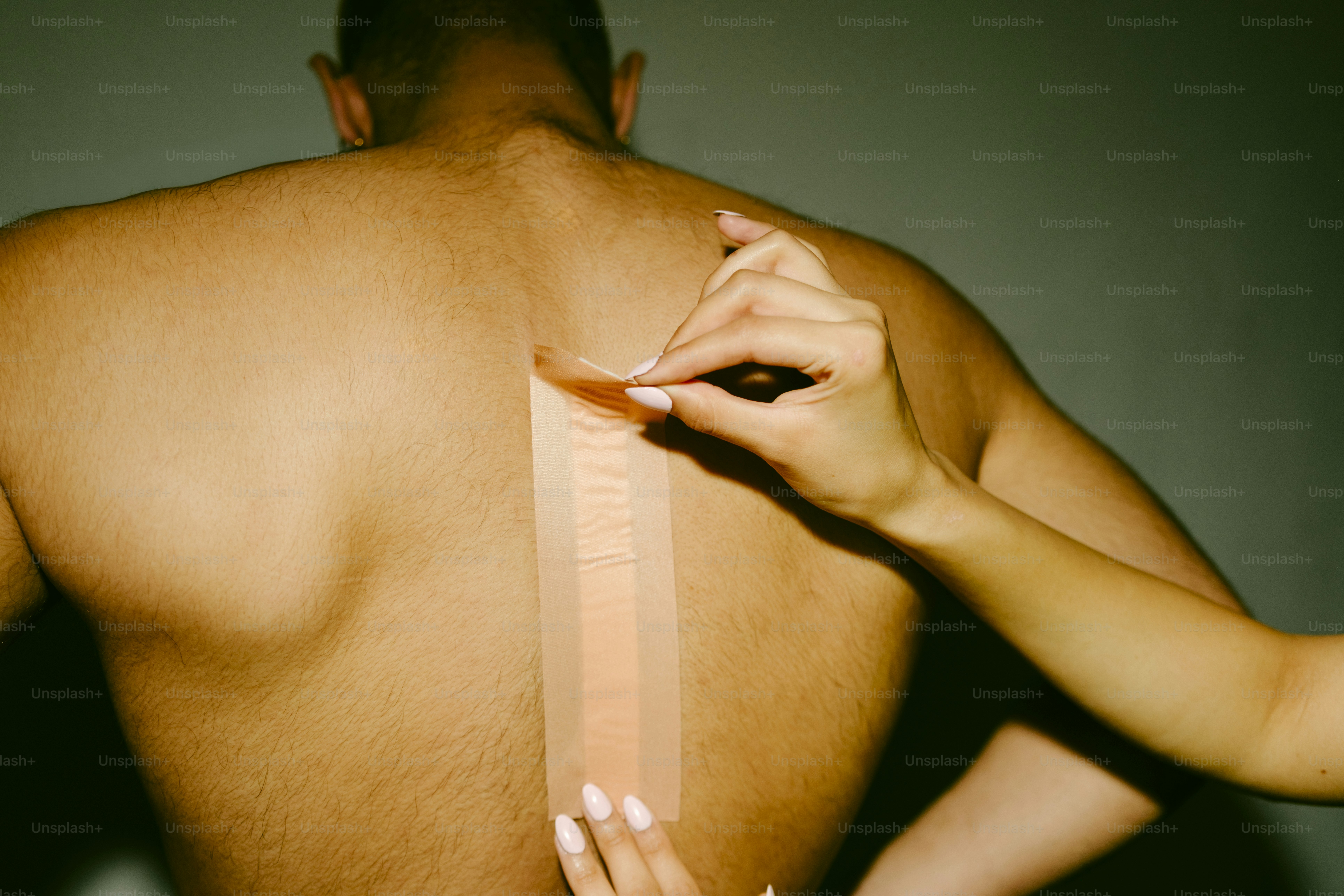 Mãos aplicando fita terapêutica nas costas de uma pessoa.