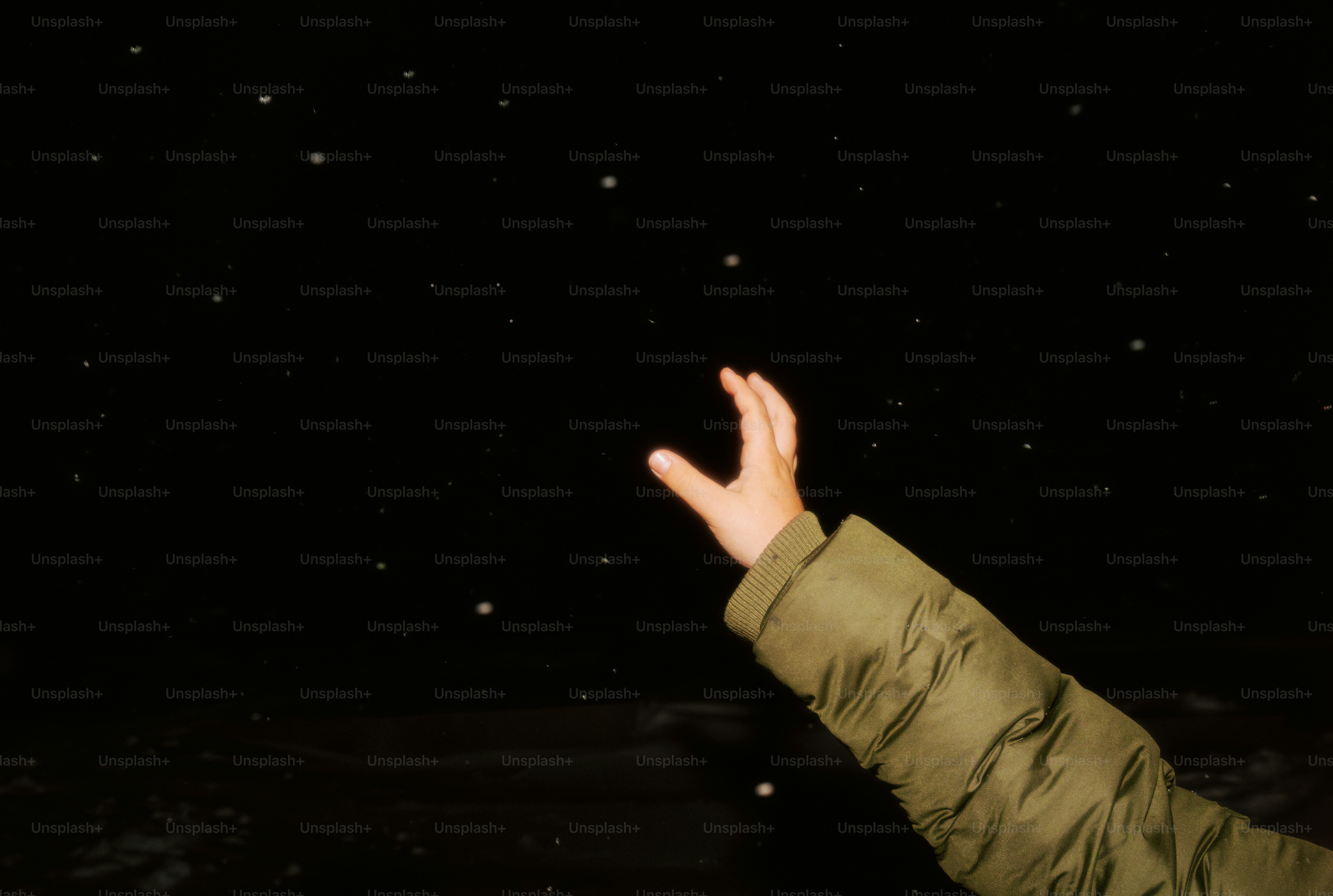 A hand reaching up towards falling snow at night.