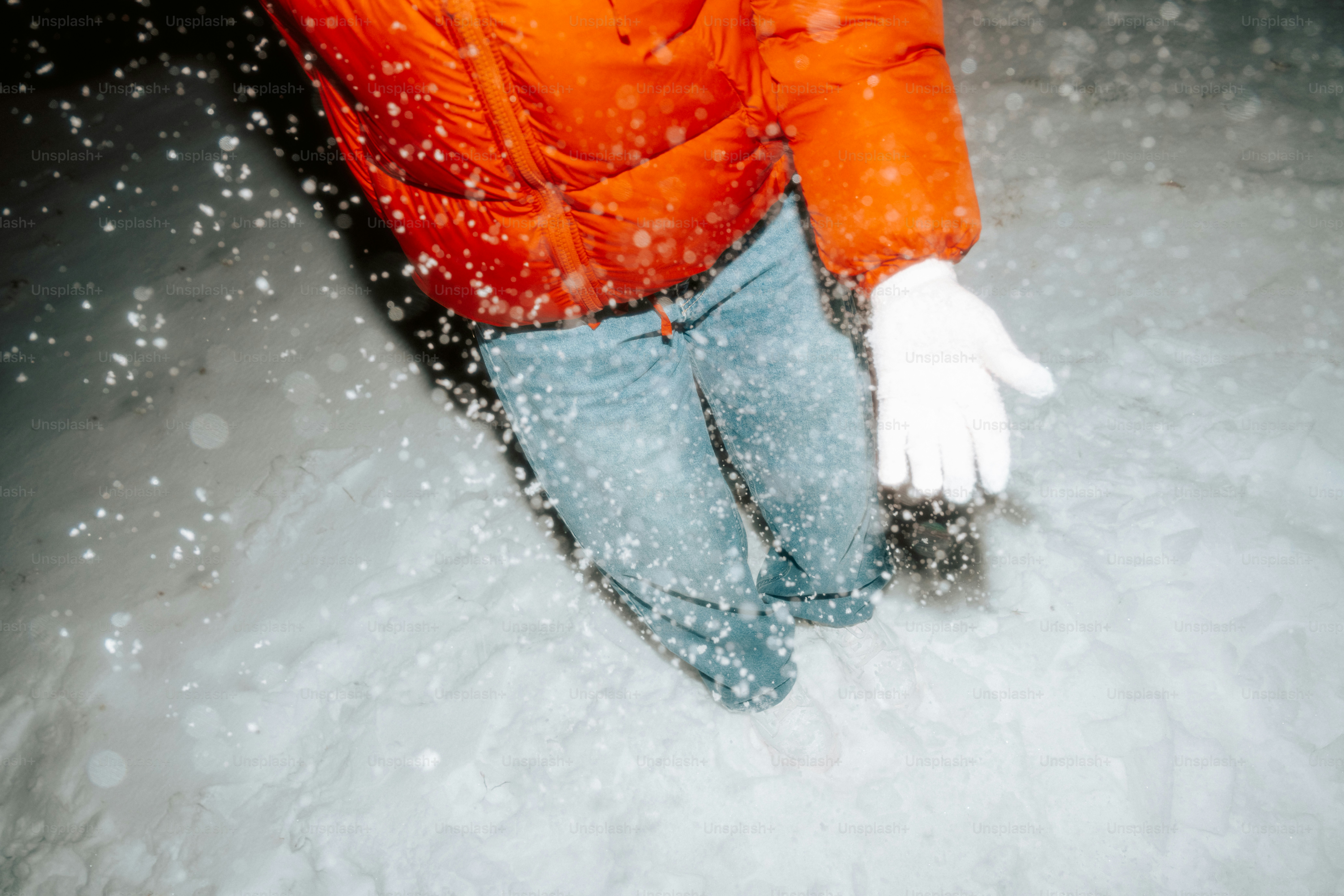 Person in orange jacket and blue jeans in snow