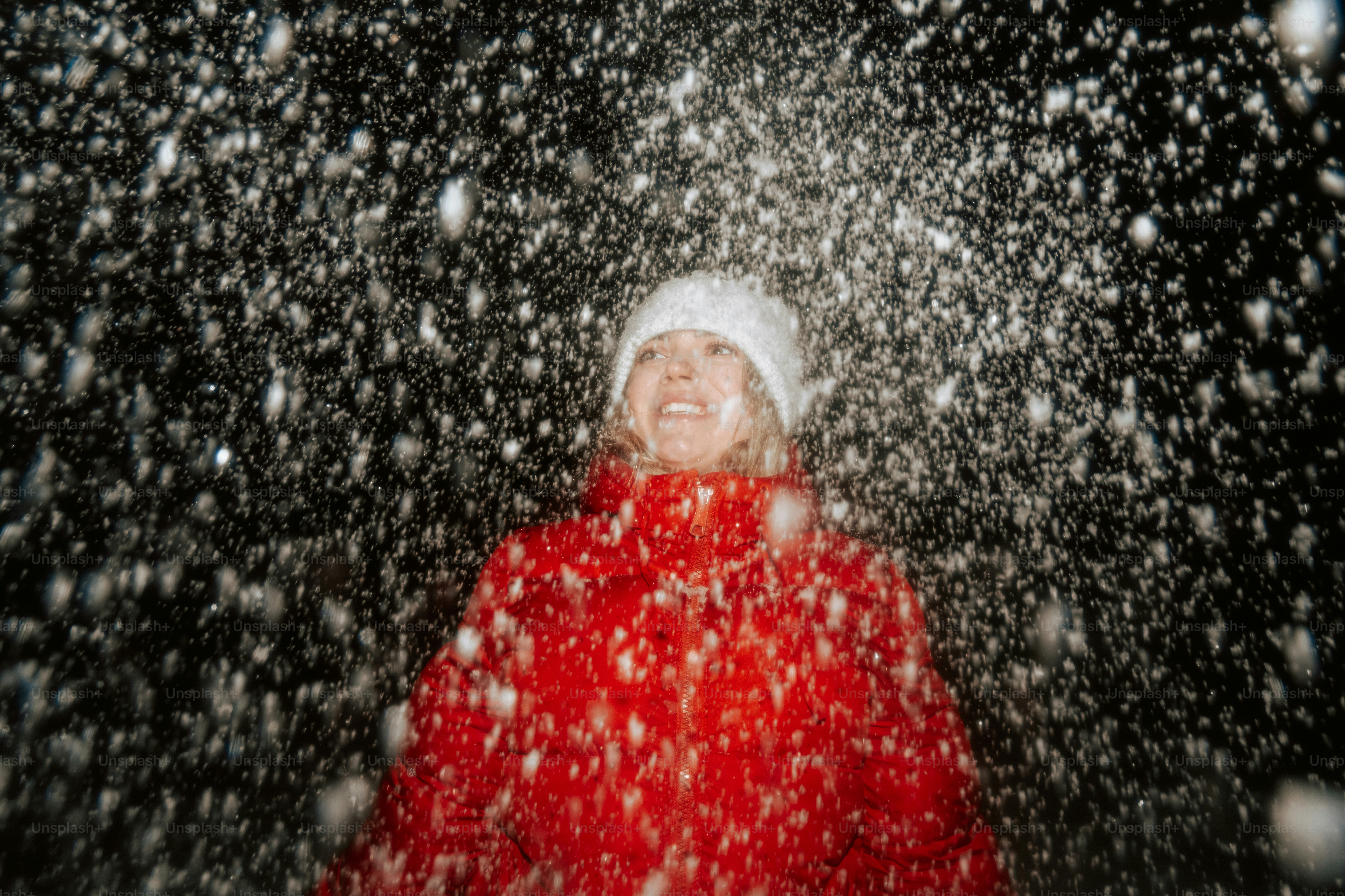 A woman in a red coat smiles in falling snow