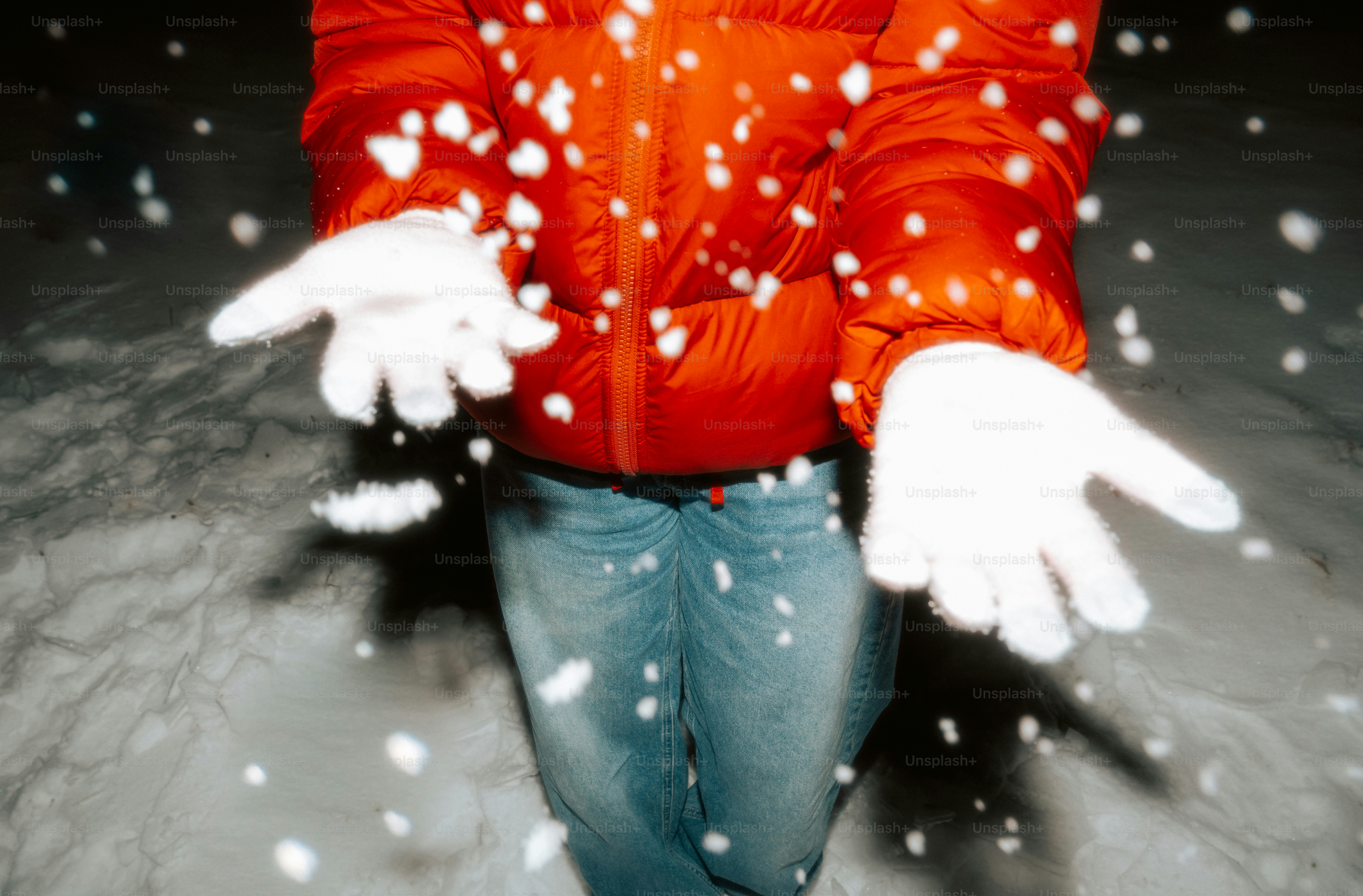 Person in orange jacket catching snowflakes with gloves.