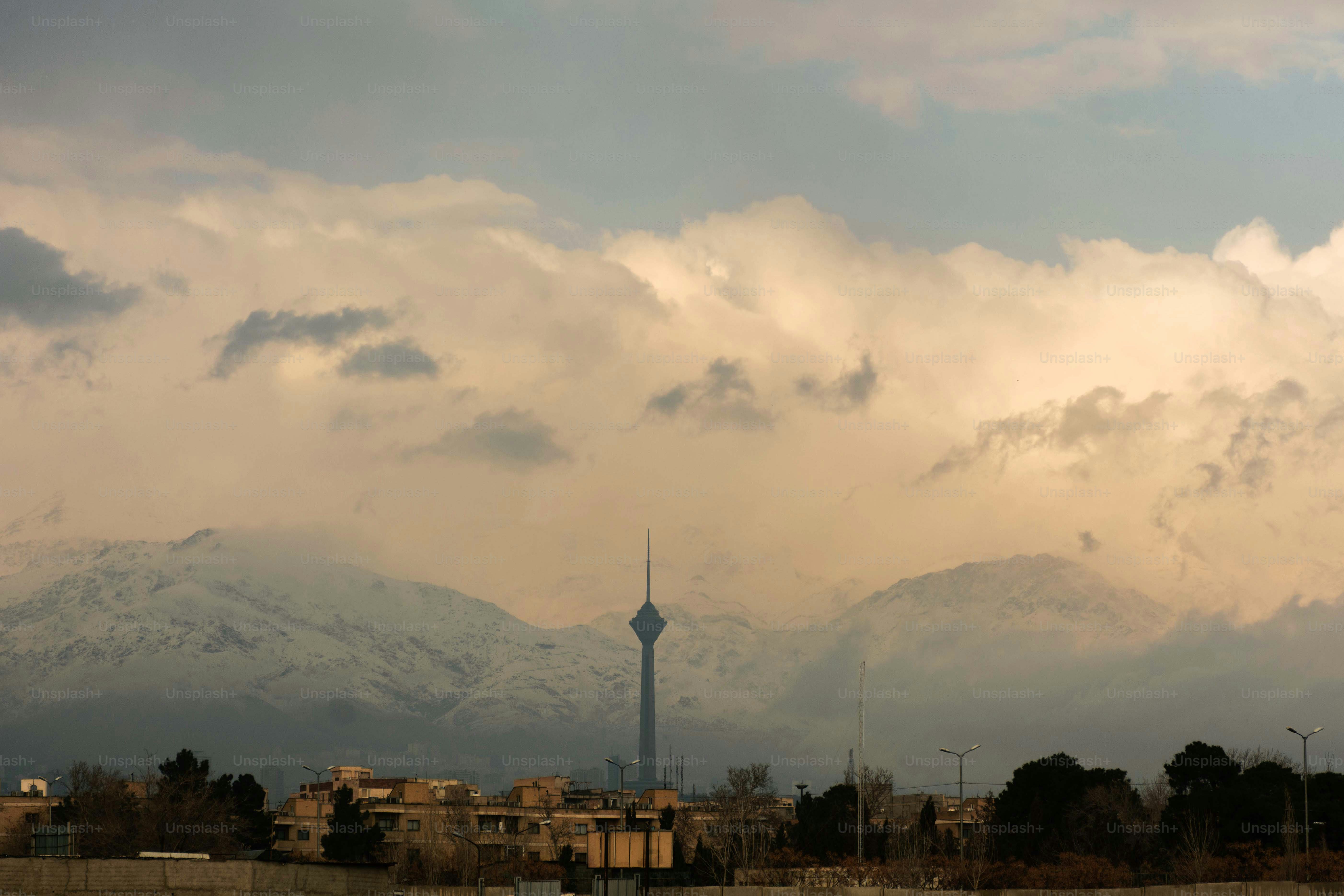 La torre Milad se alza sobre montañas nevadas y nubes