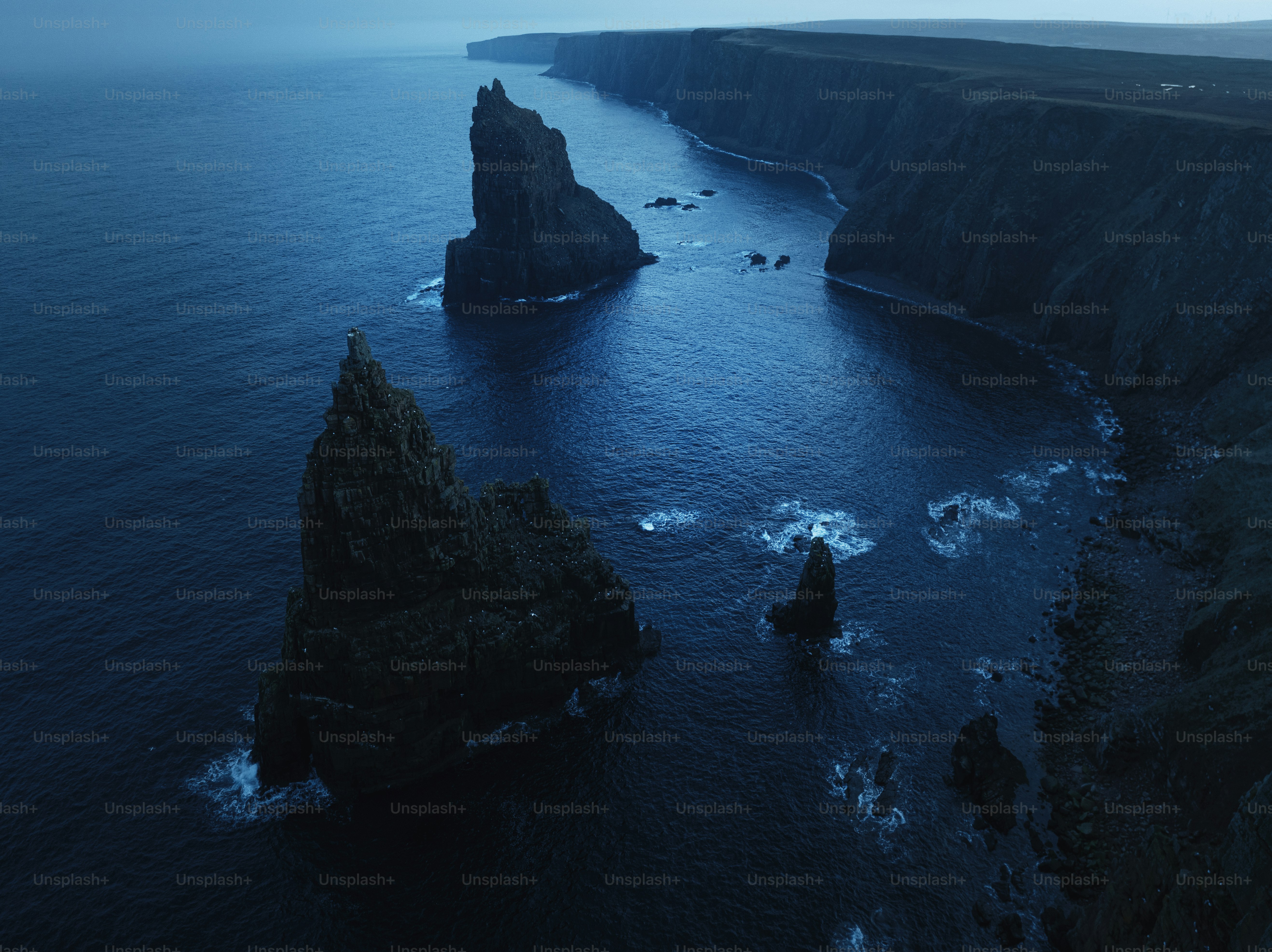 Dramatic sea stacks rise from dark ocean waters at dusk.