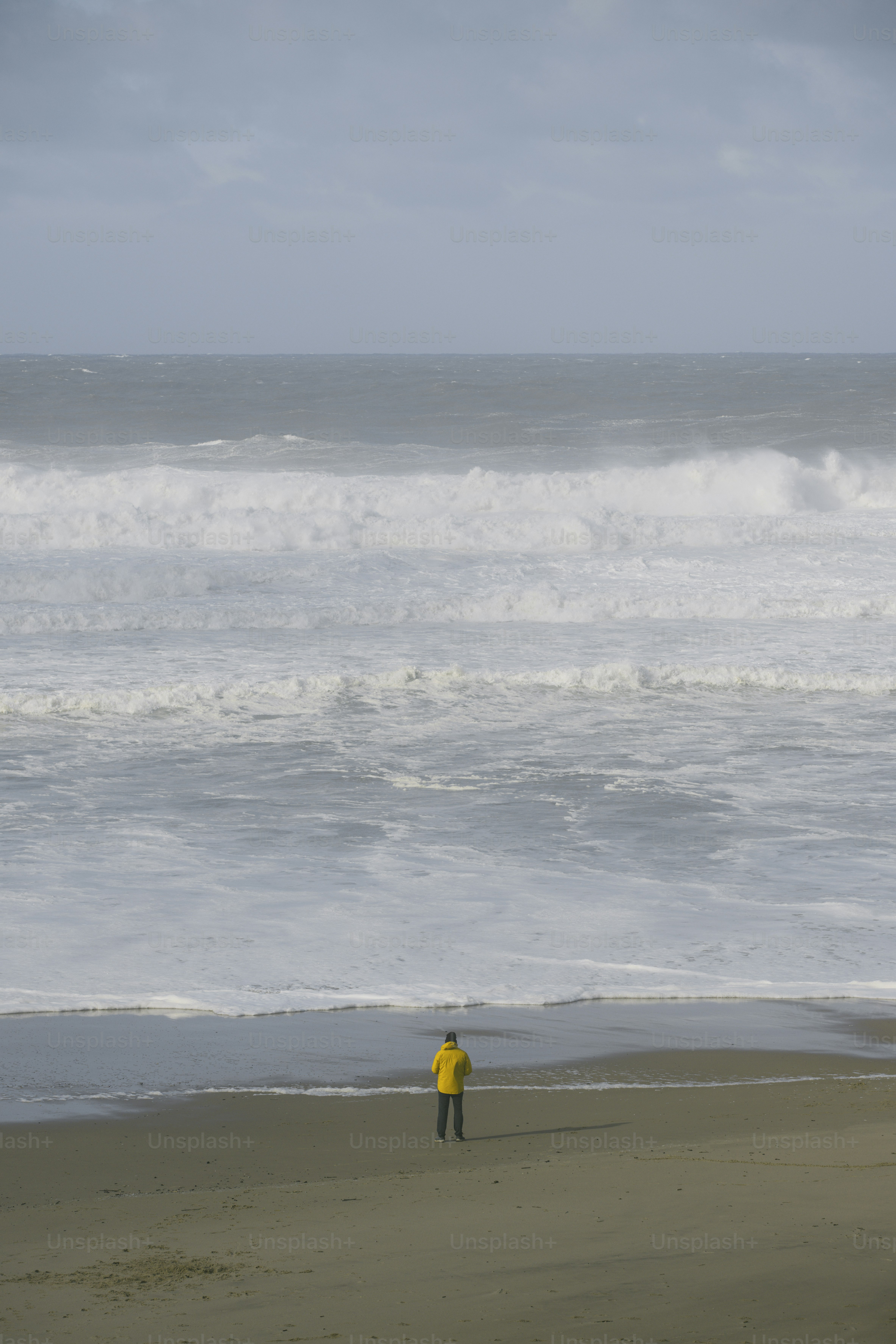 黄色いジャケットを着た男が海に面した浜辺に立っている