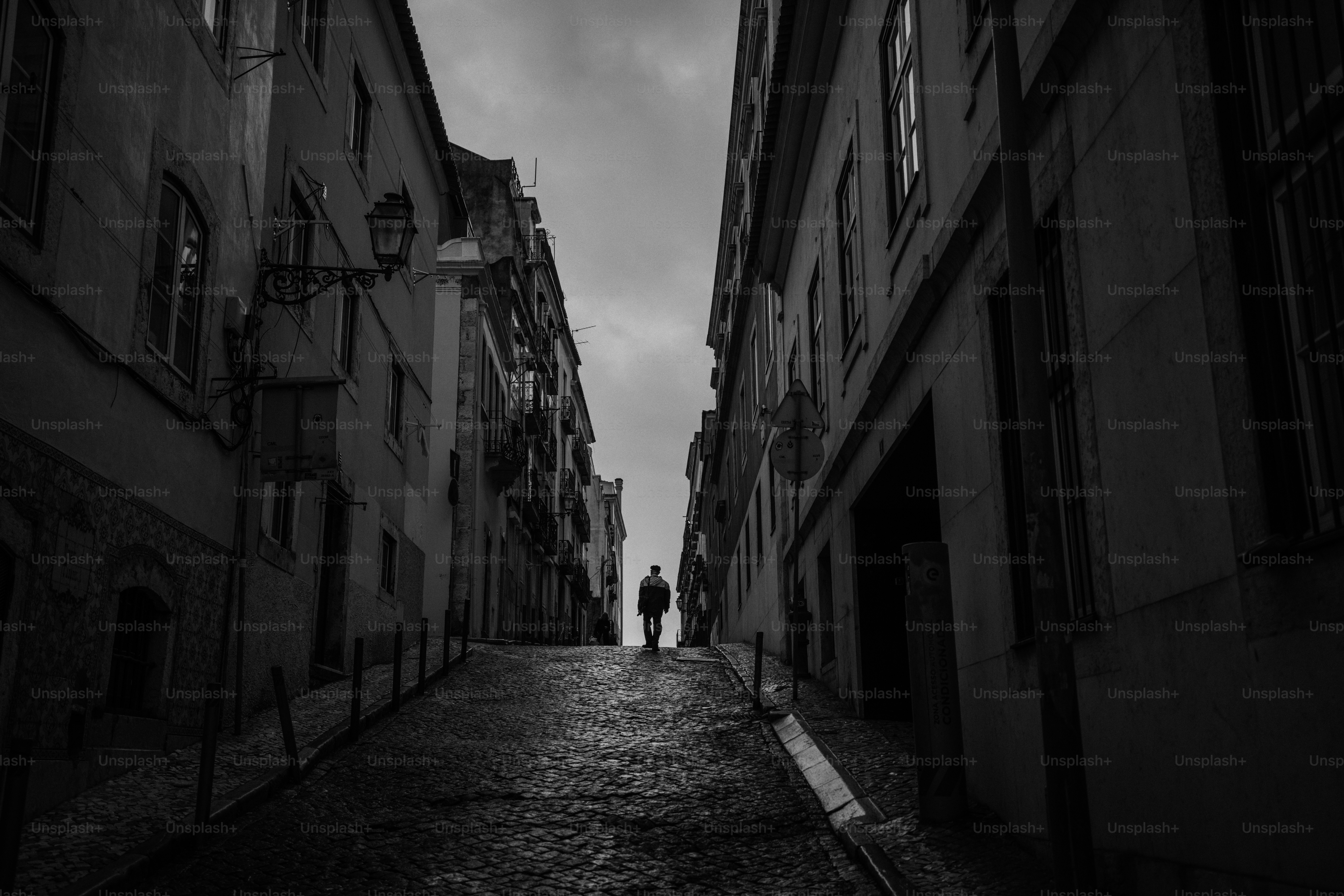 Uma figura solitária caminha por uma rua de paralelepípedos.