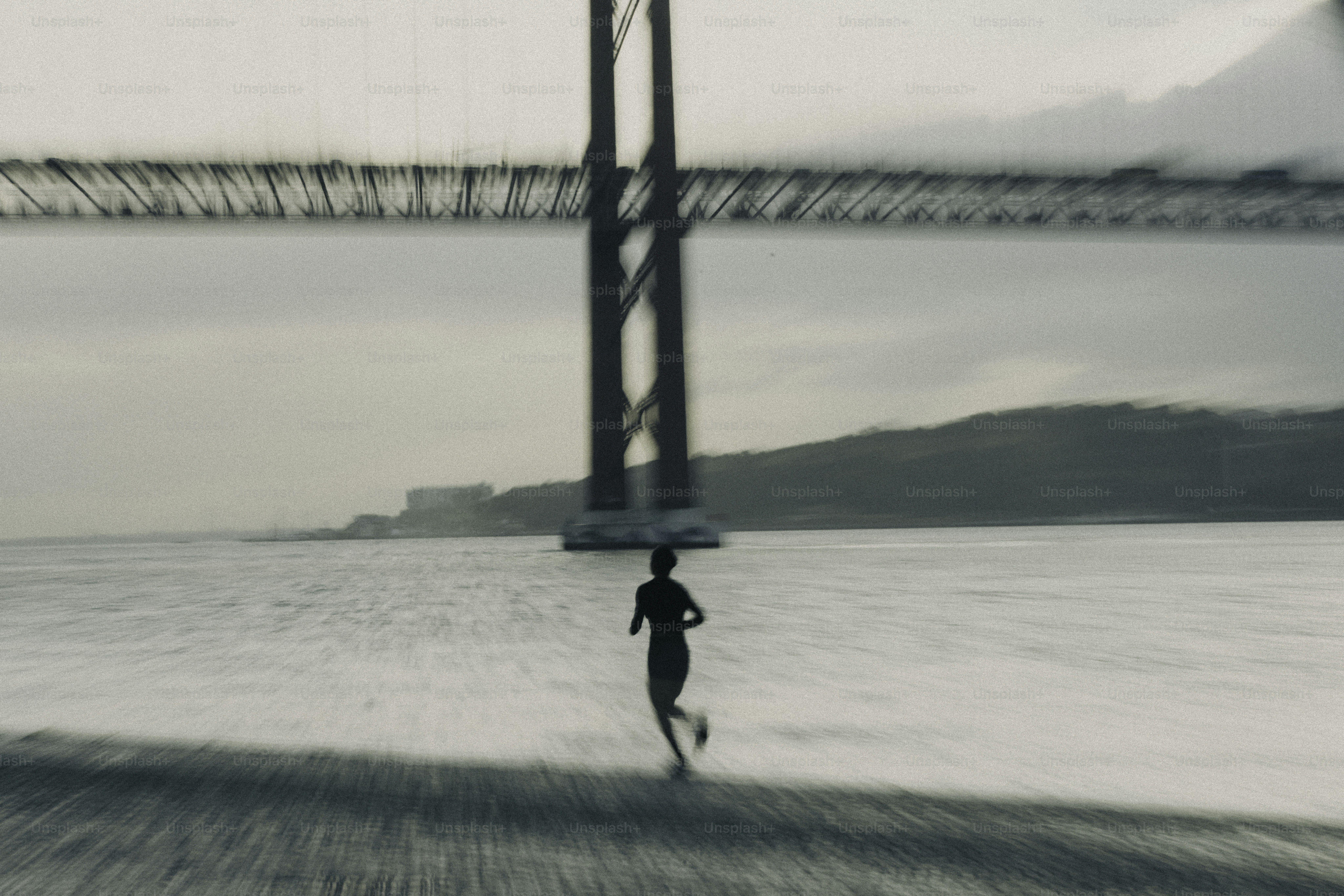 A lone runner jogs along the water under a bridge.