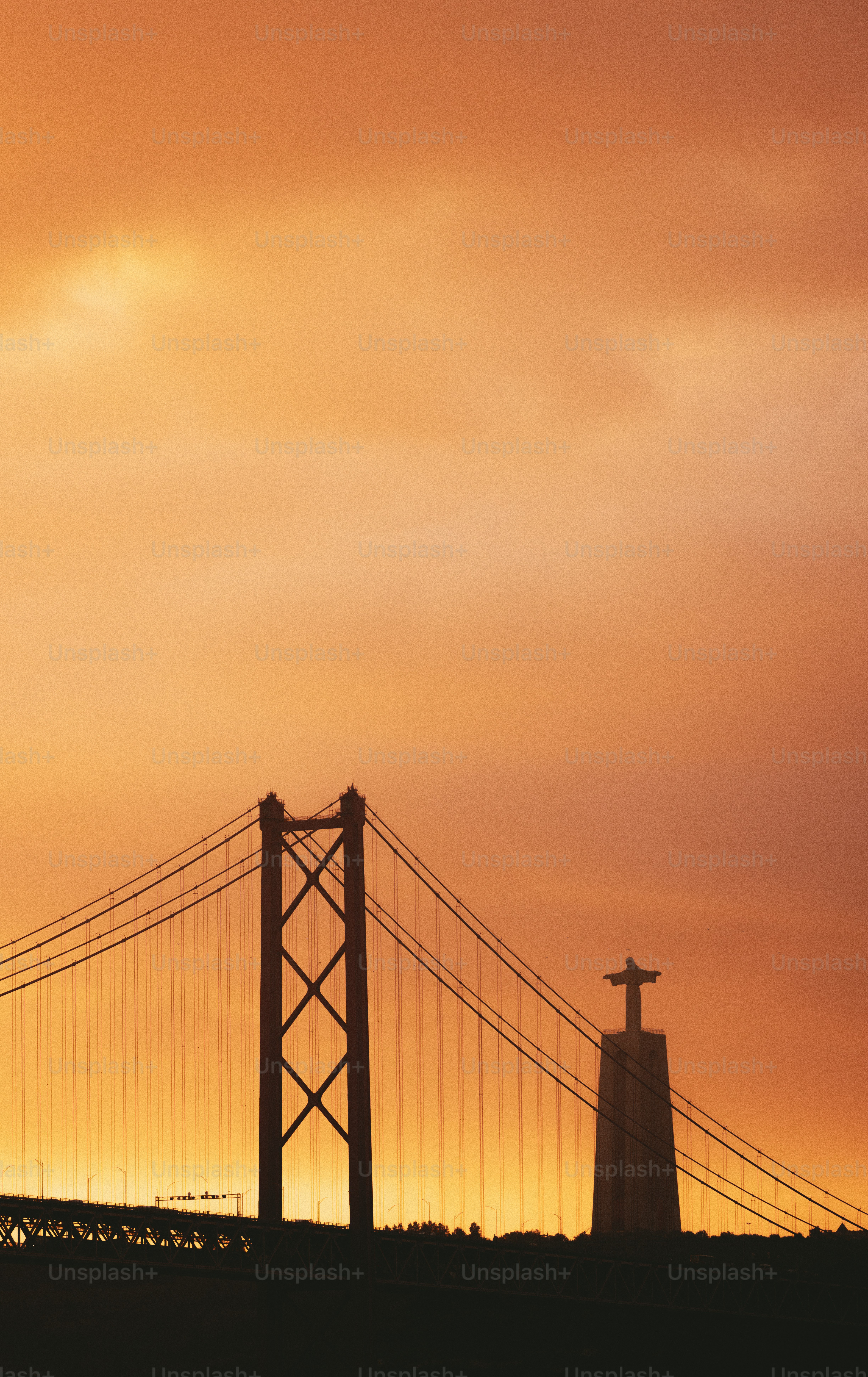 Bridge and statue silhouetted against a vibrant sunset.