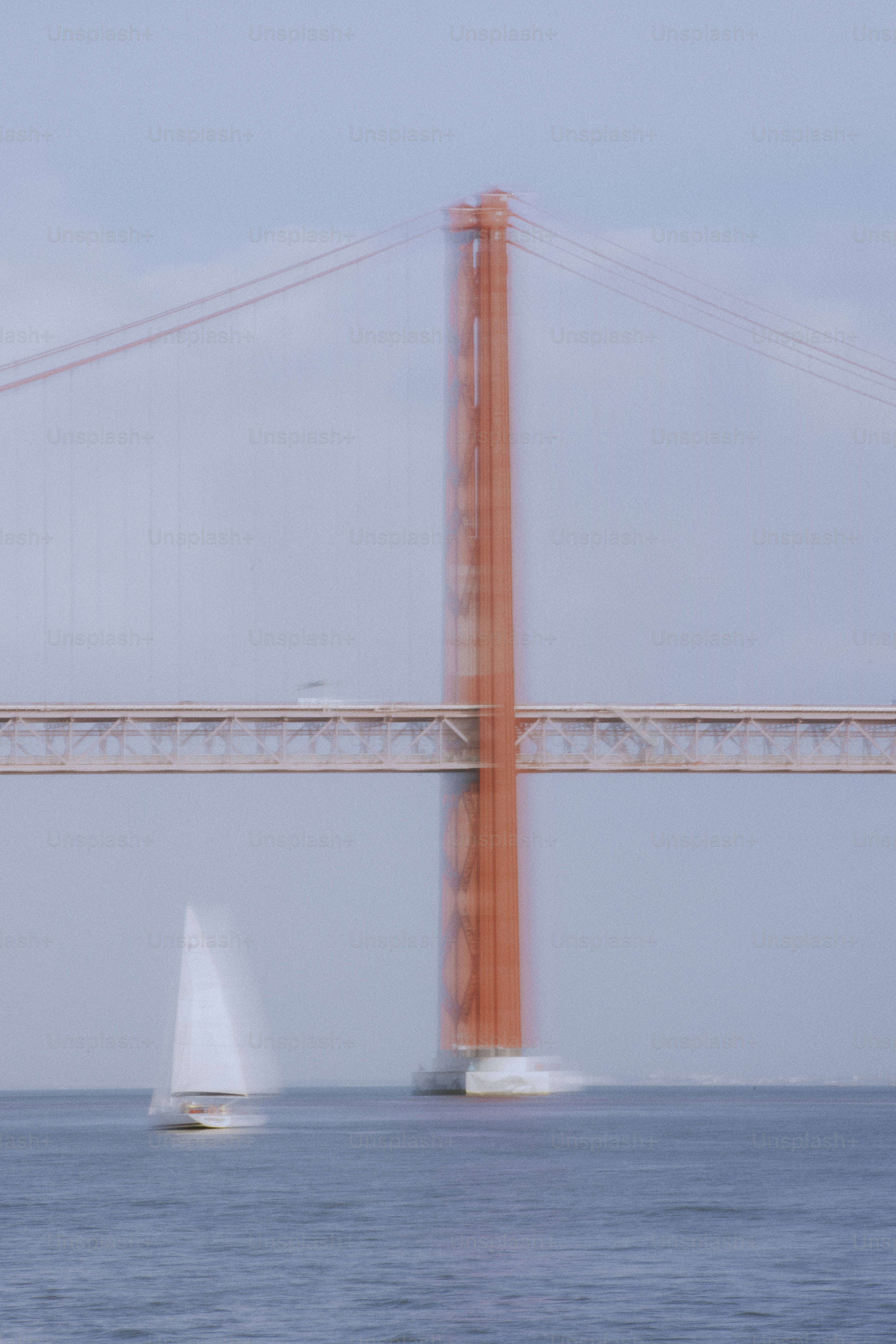 Red suspension bridge over blue water with sailboat