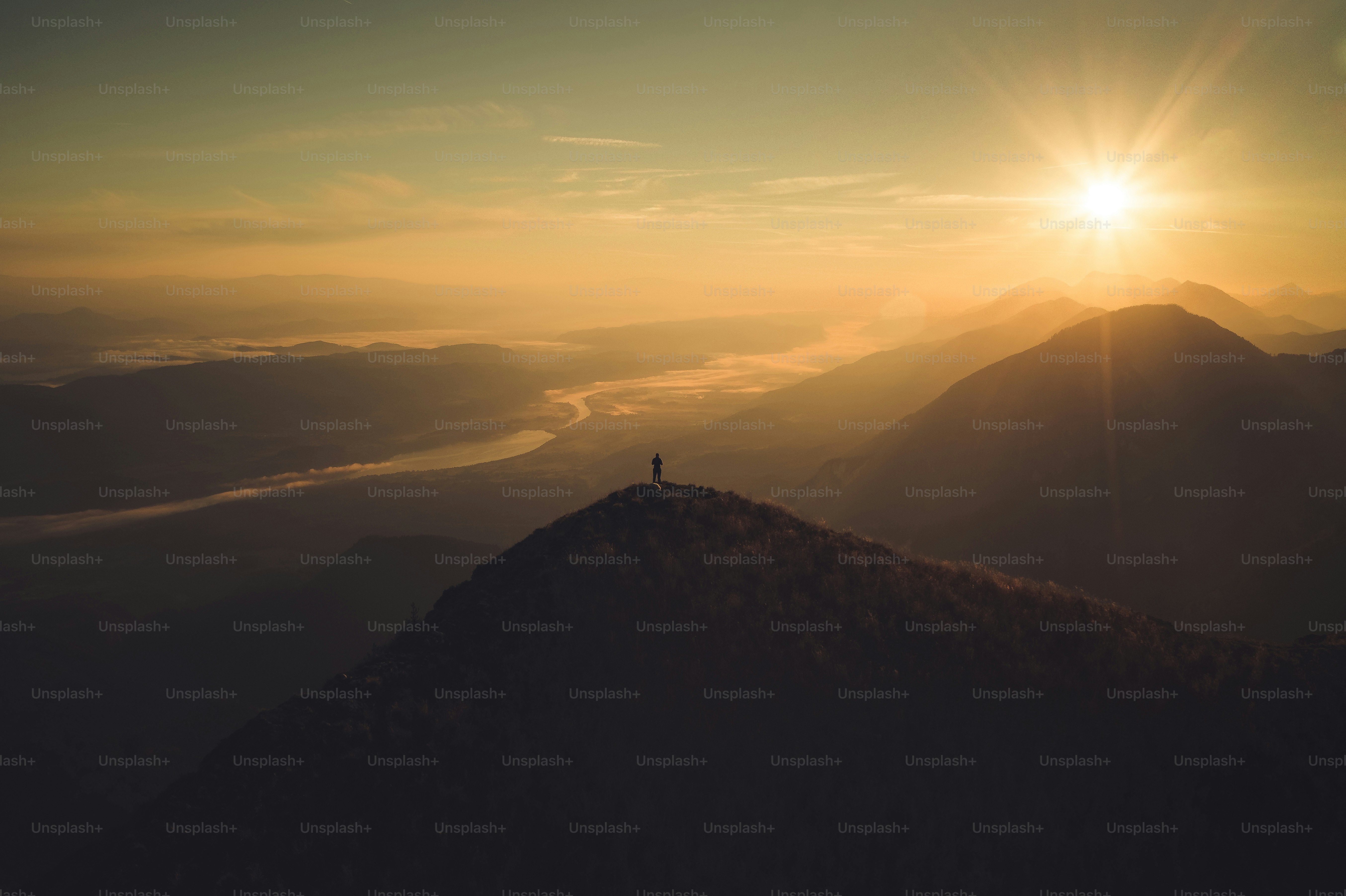 Eine einzelne Gestalt steht bei Sonnenaufgang auf einem Berggipfel.