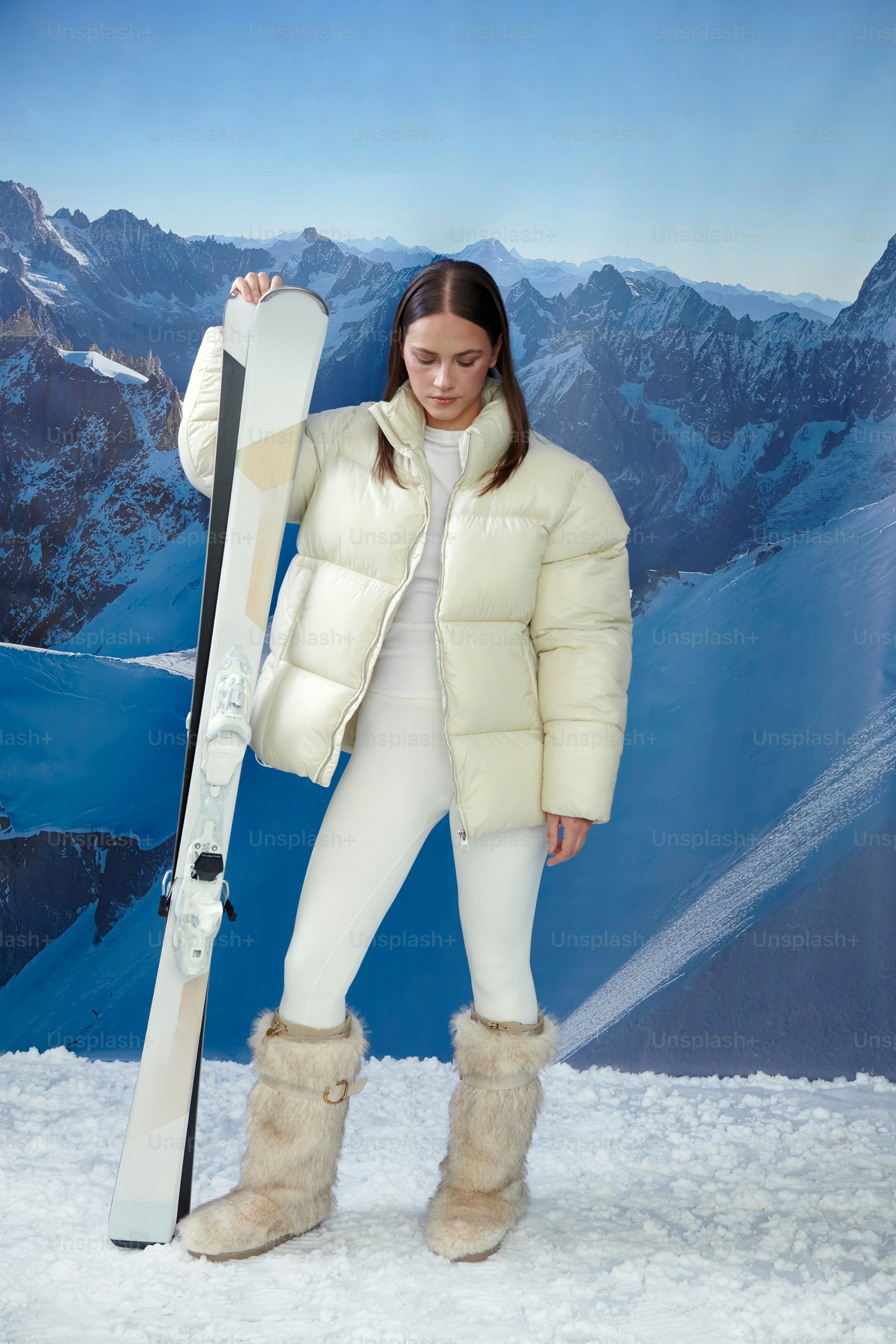 白いスキーウェアを着た女性が雪山を描いたスキーを持っている