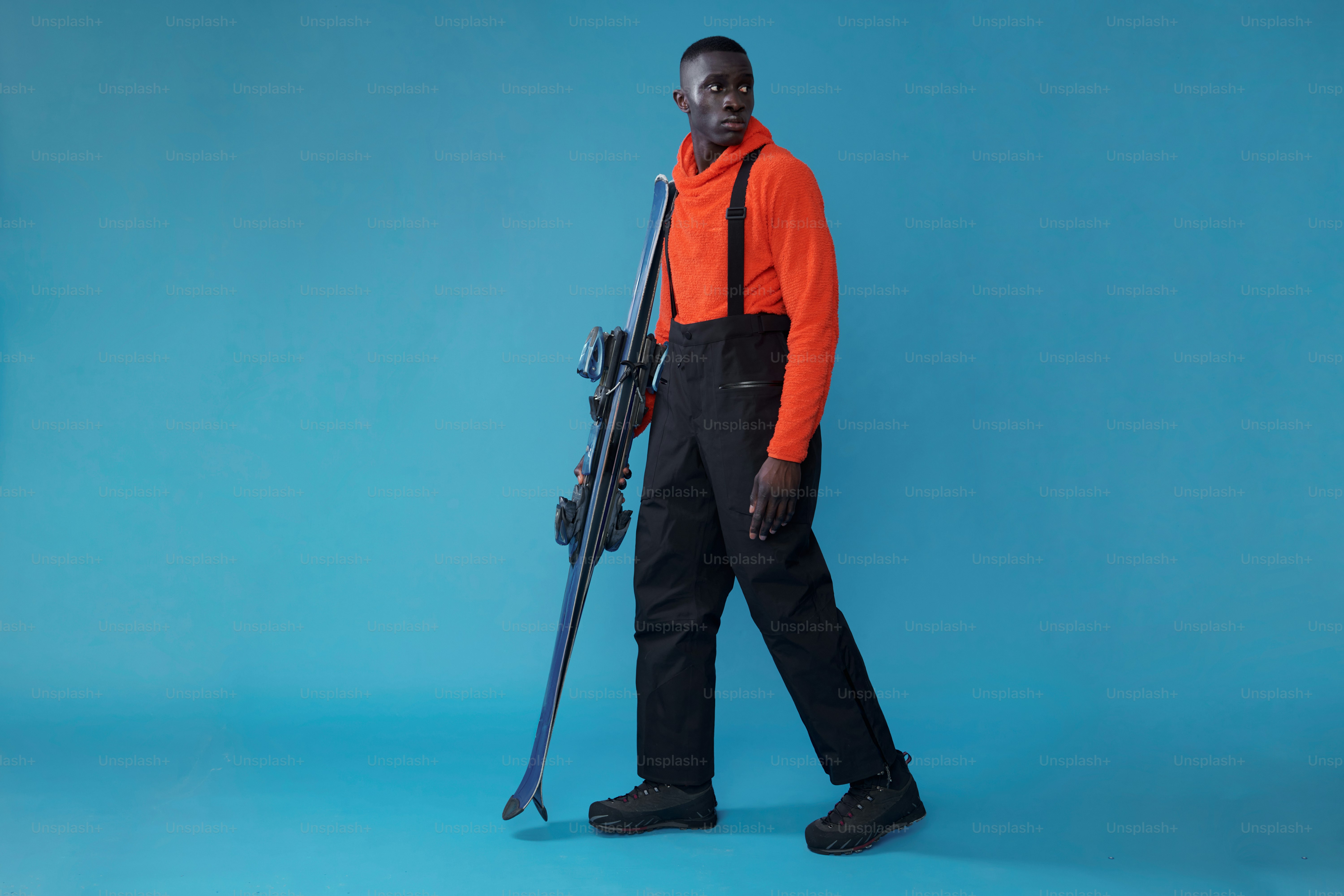 オレンジ色のシャツを着た男性が青い背景にスキー板を持っている