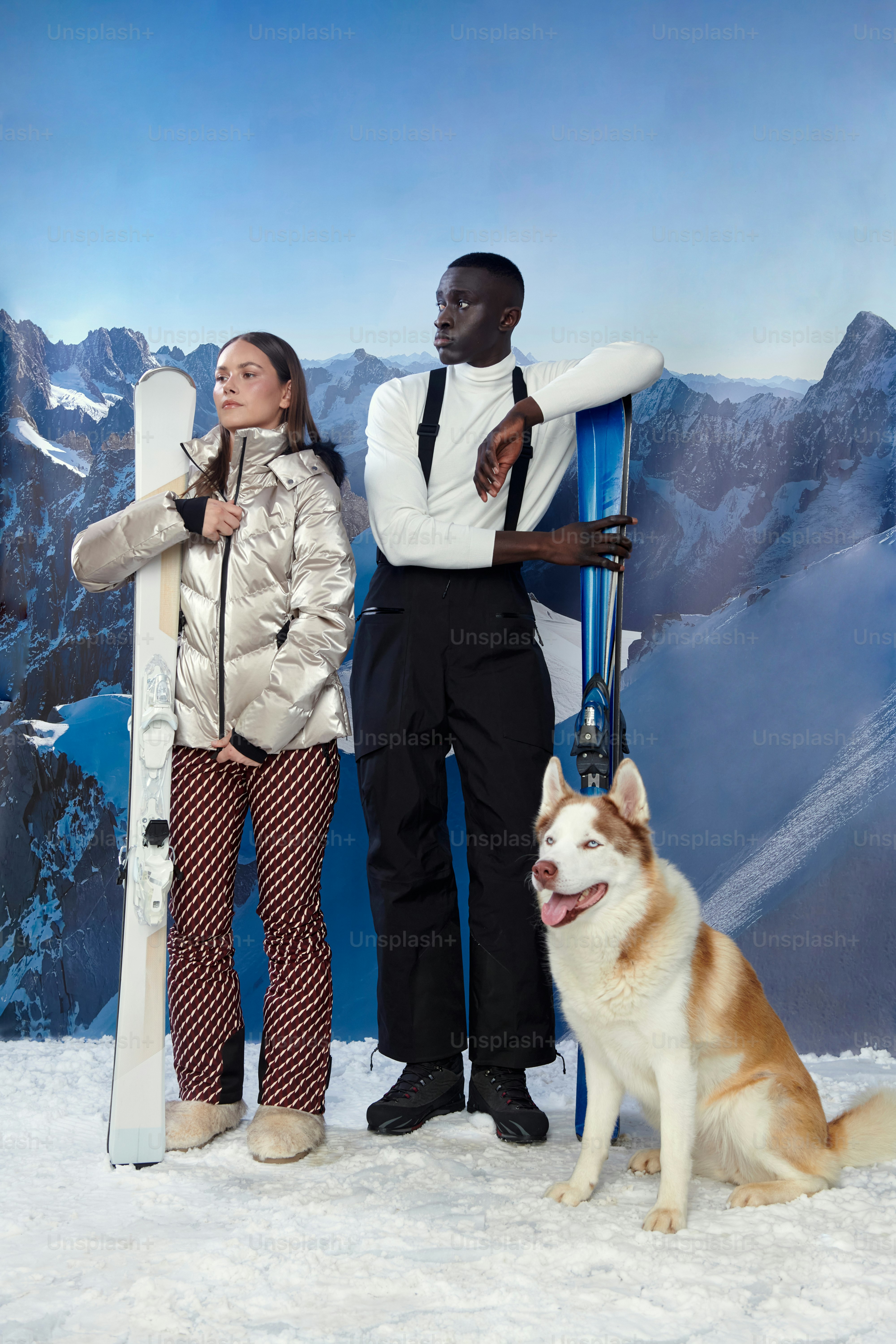 雪山でスキーヤー2人とハスキー1人がポーズをとる。