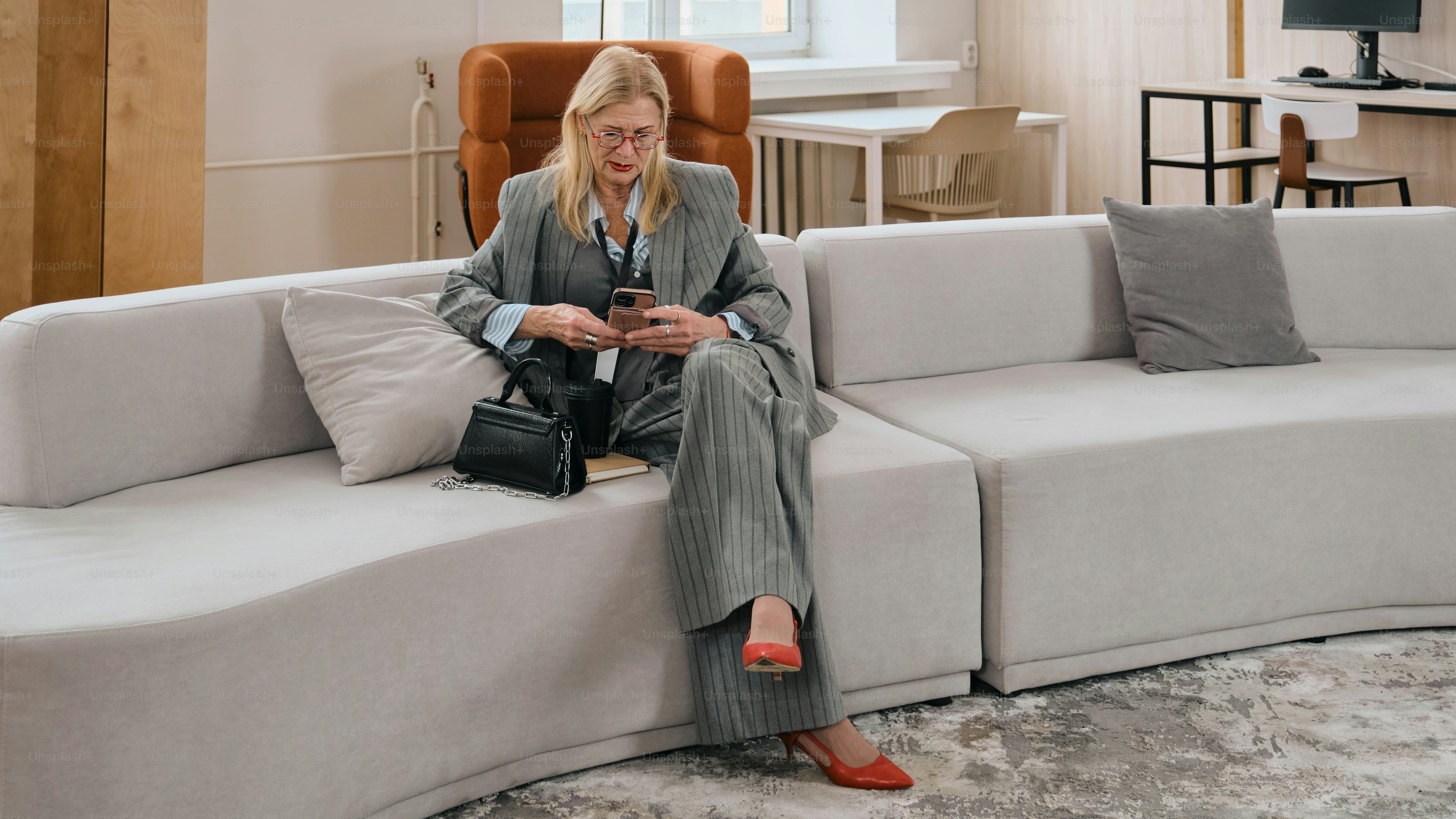 Frau im Anzug sitzt auf einem Sofa und benutzt das Handy