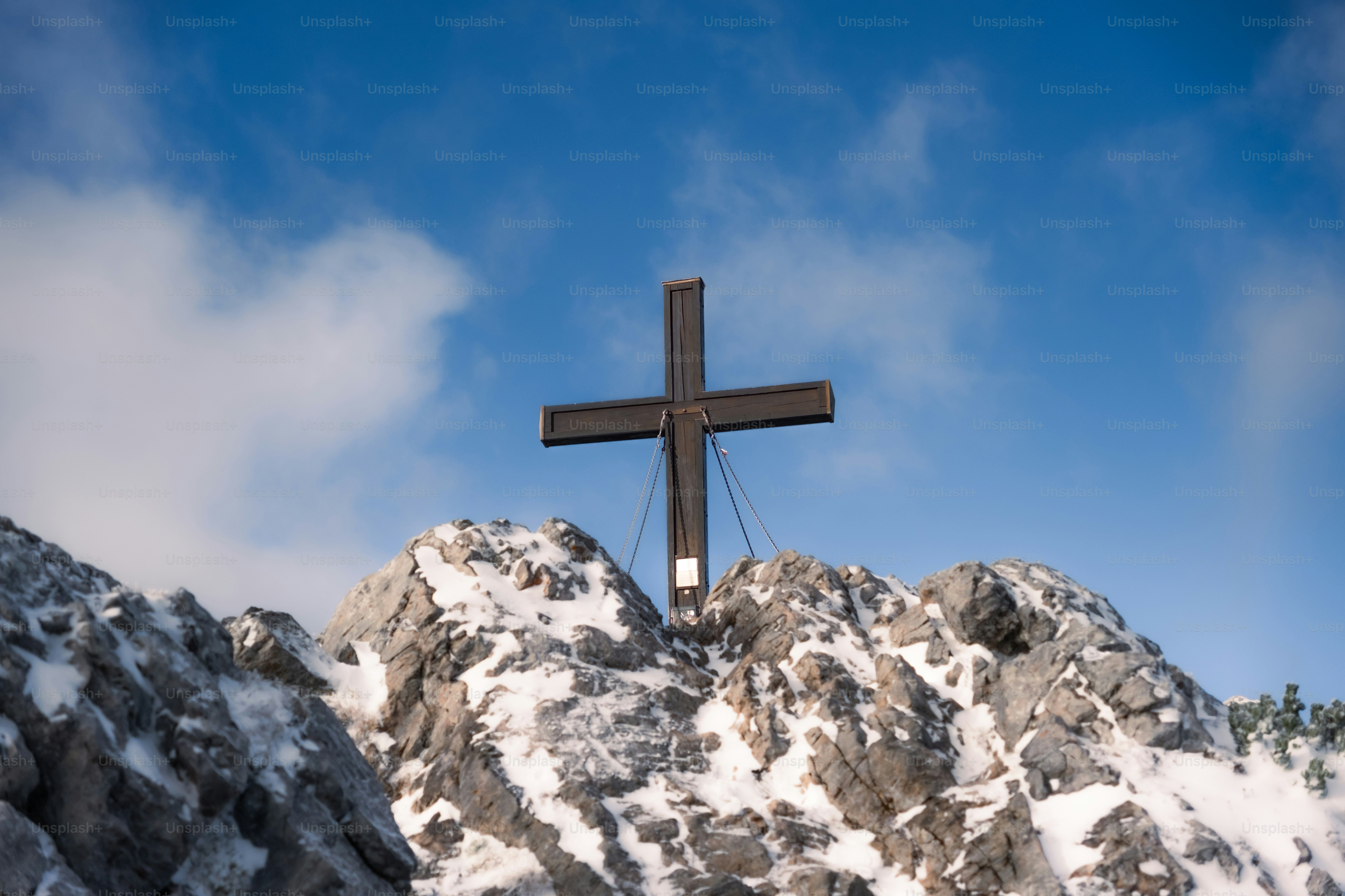 A large cross stands atop a snow-covered mountain peak.
