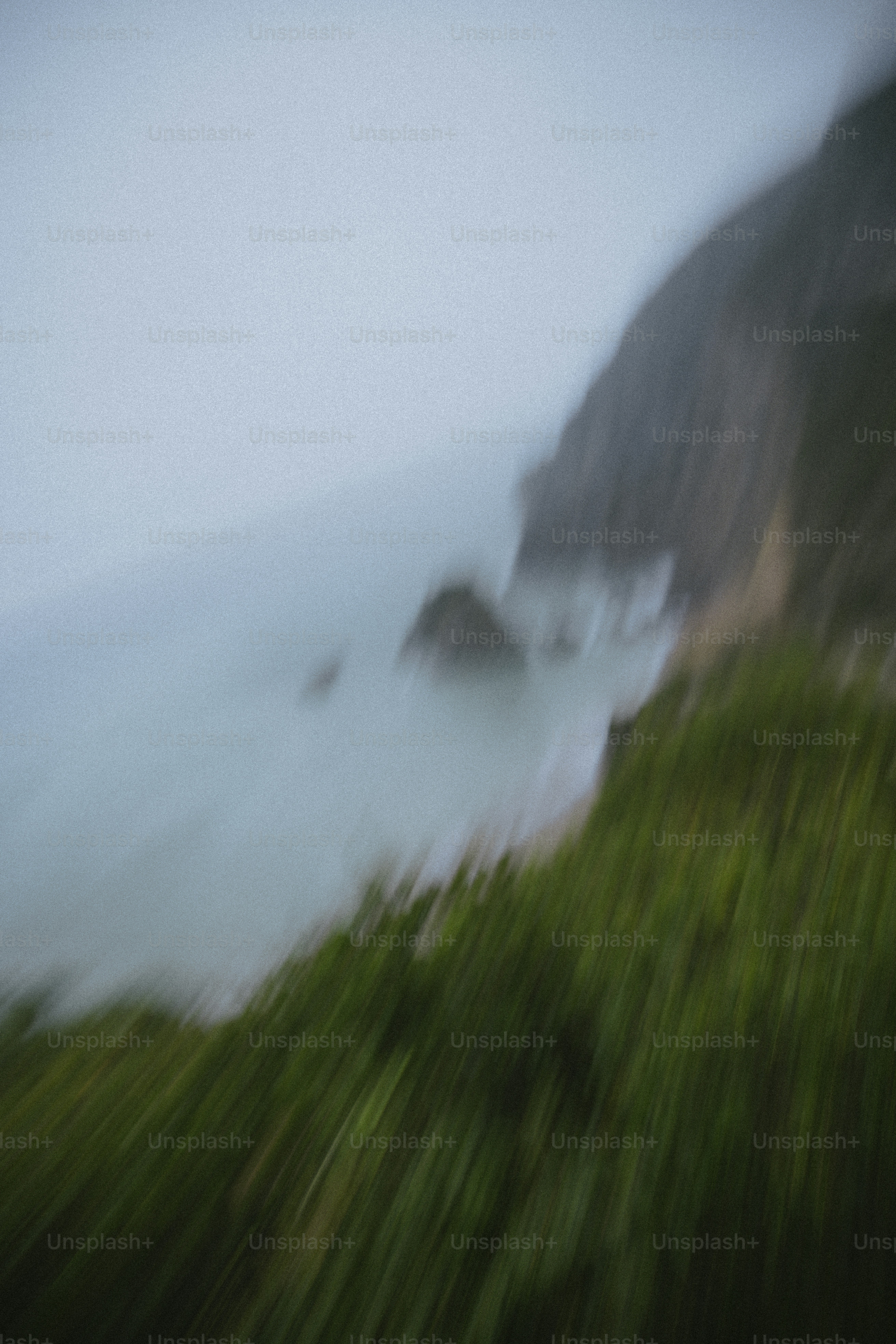 Blurry coastal cliffside with green grass and ocean