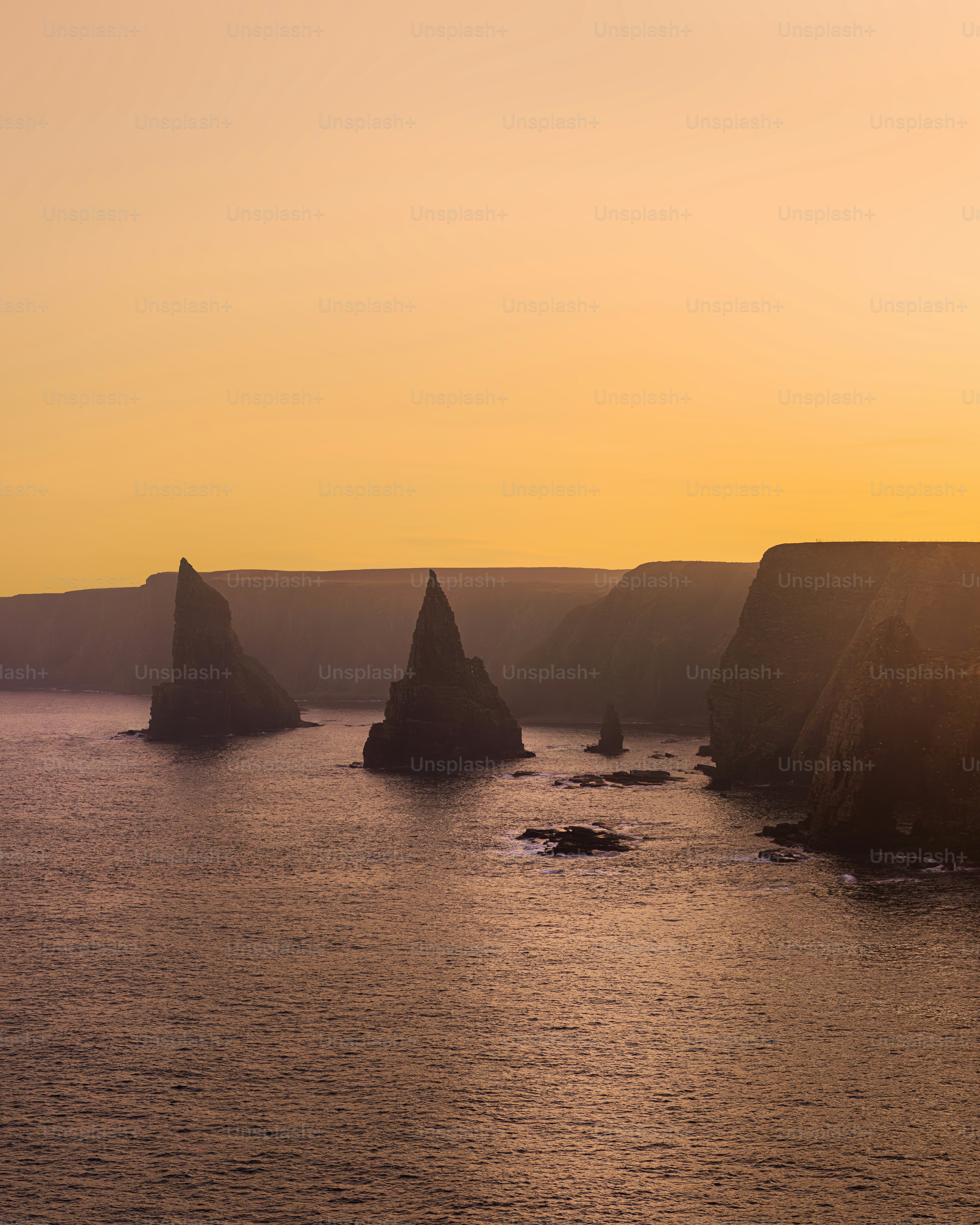 Jagged sea stacks rise from the ocean at sunset.