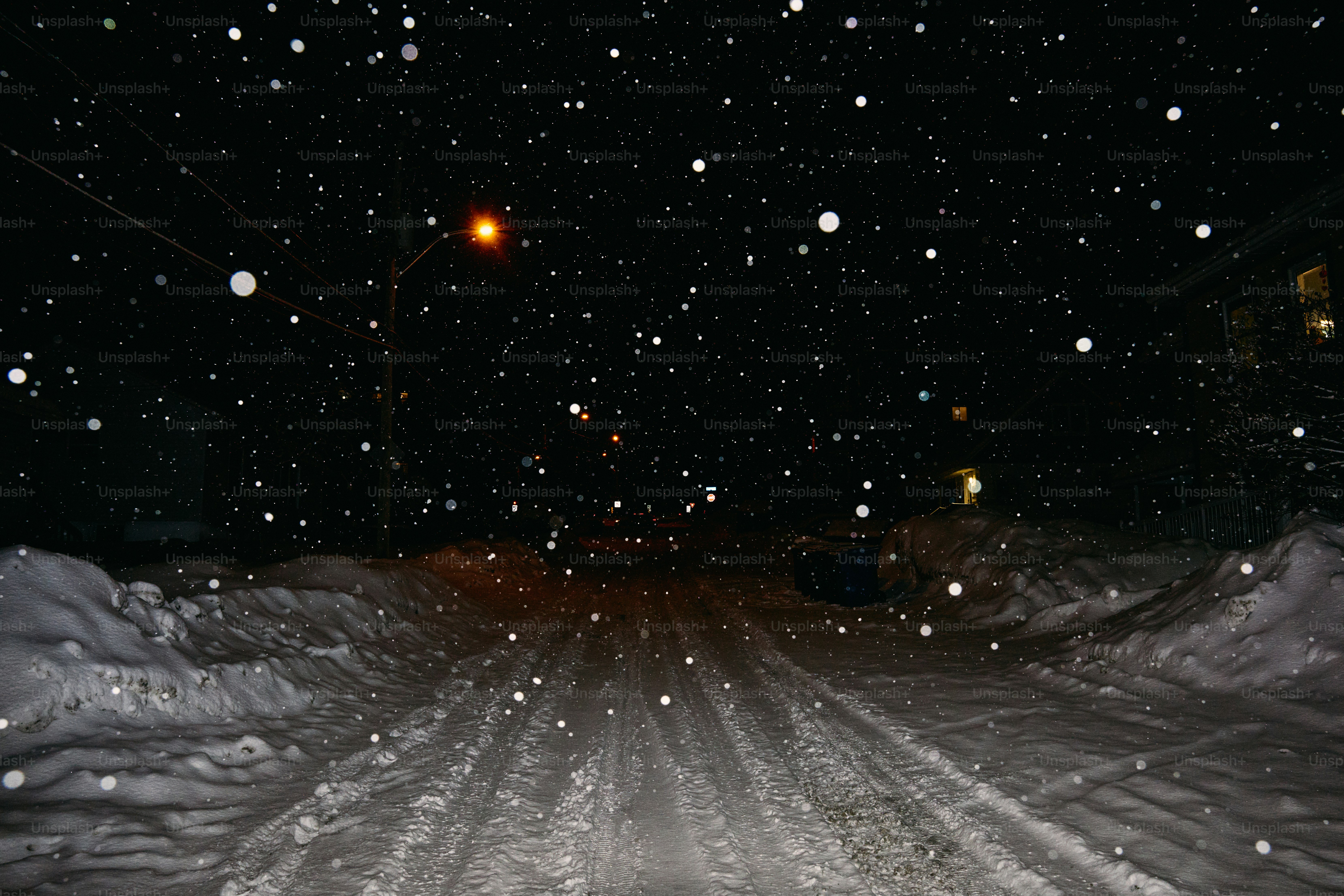 Snow falling on a dark, snowy road at night.