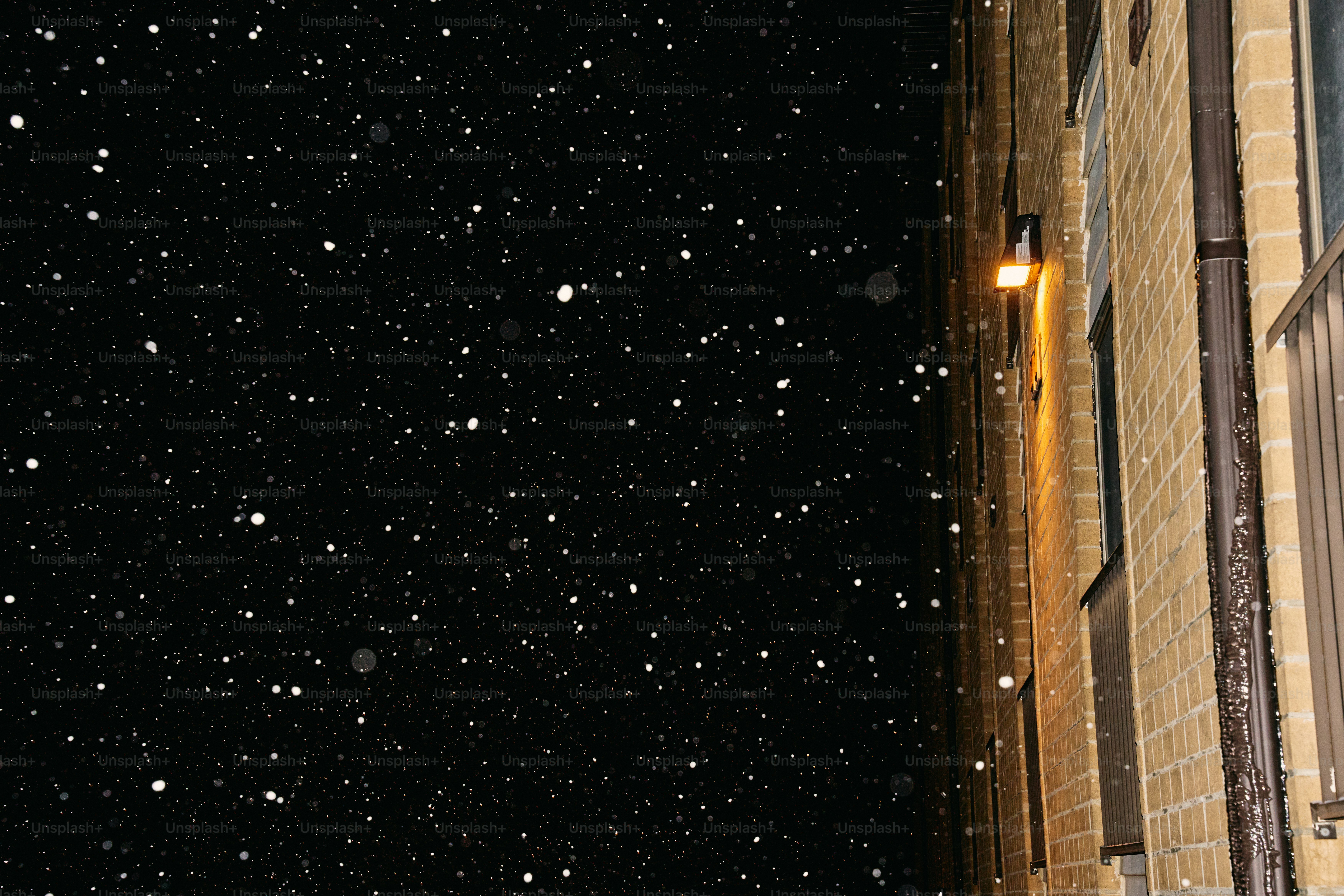 Snow falling at night next to a brick building.