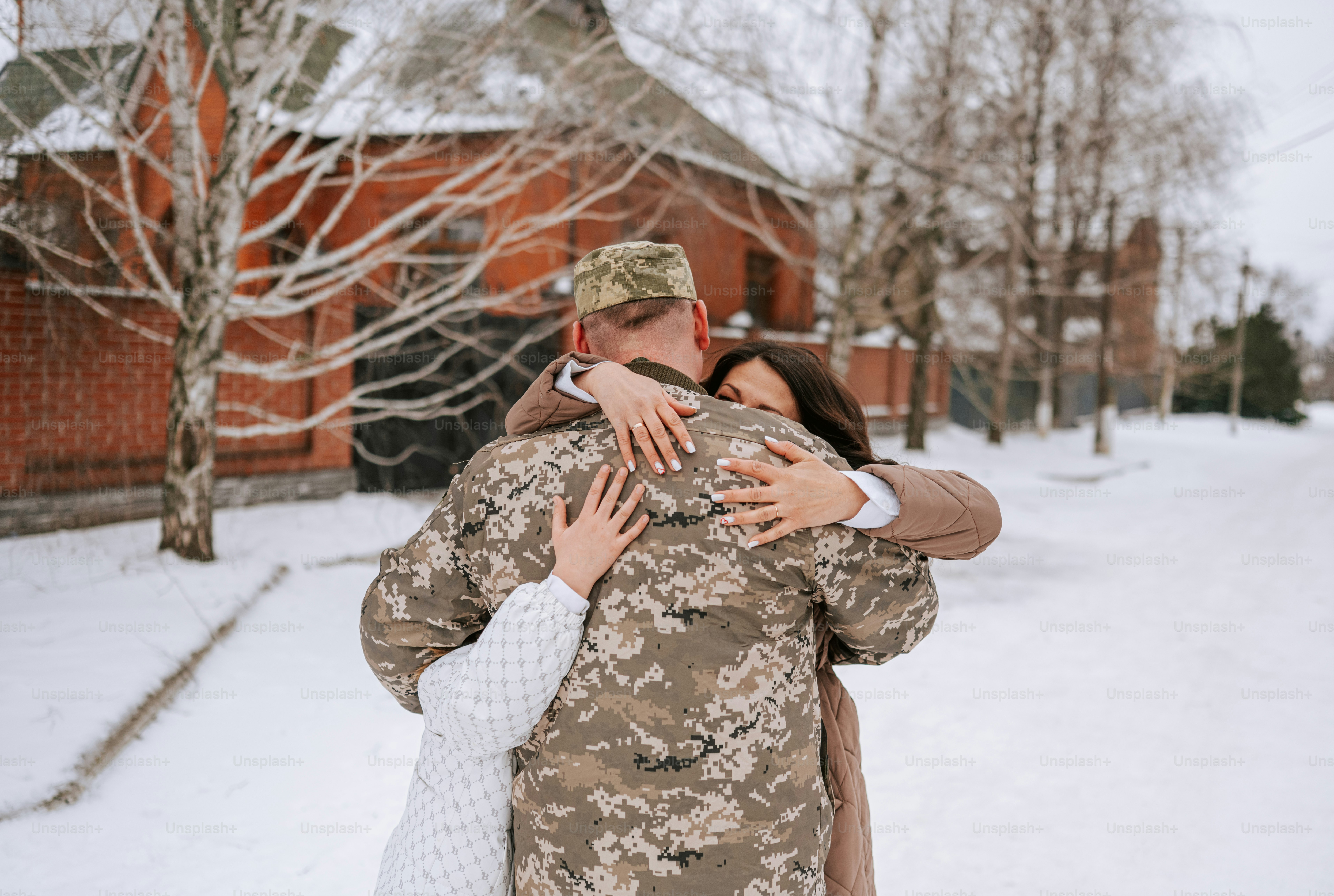 Soldat en uniforme camouflage serrant sa famille dans ses bras dans la neige