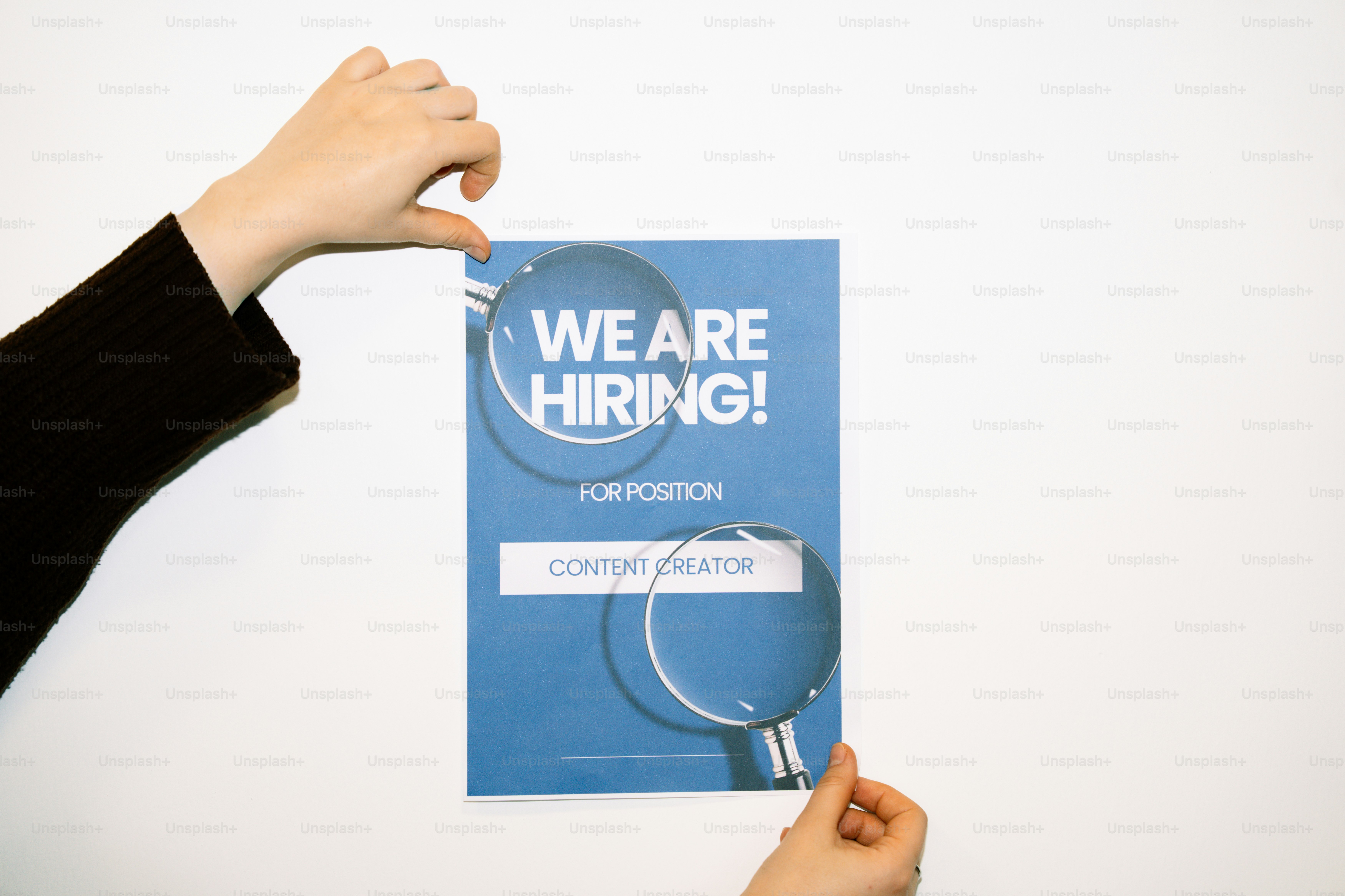 Des mains tenant un panneau « nous recrutons ! » avec une loupe.