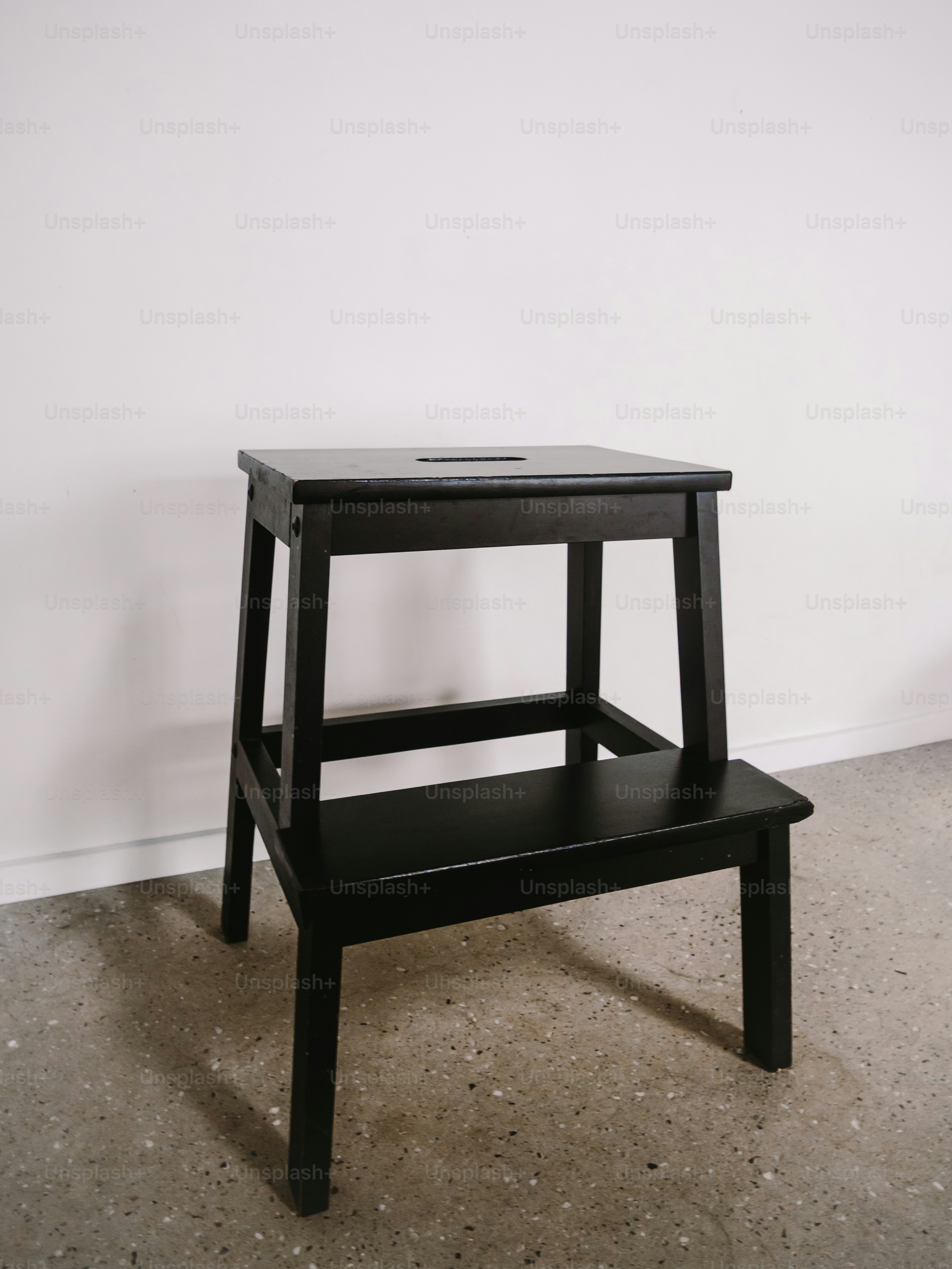 Un taburete de madera negra contra una pared blanca.