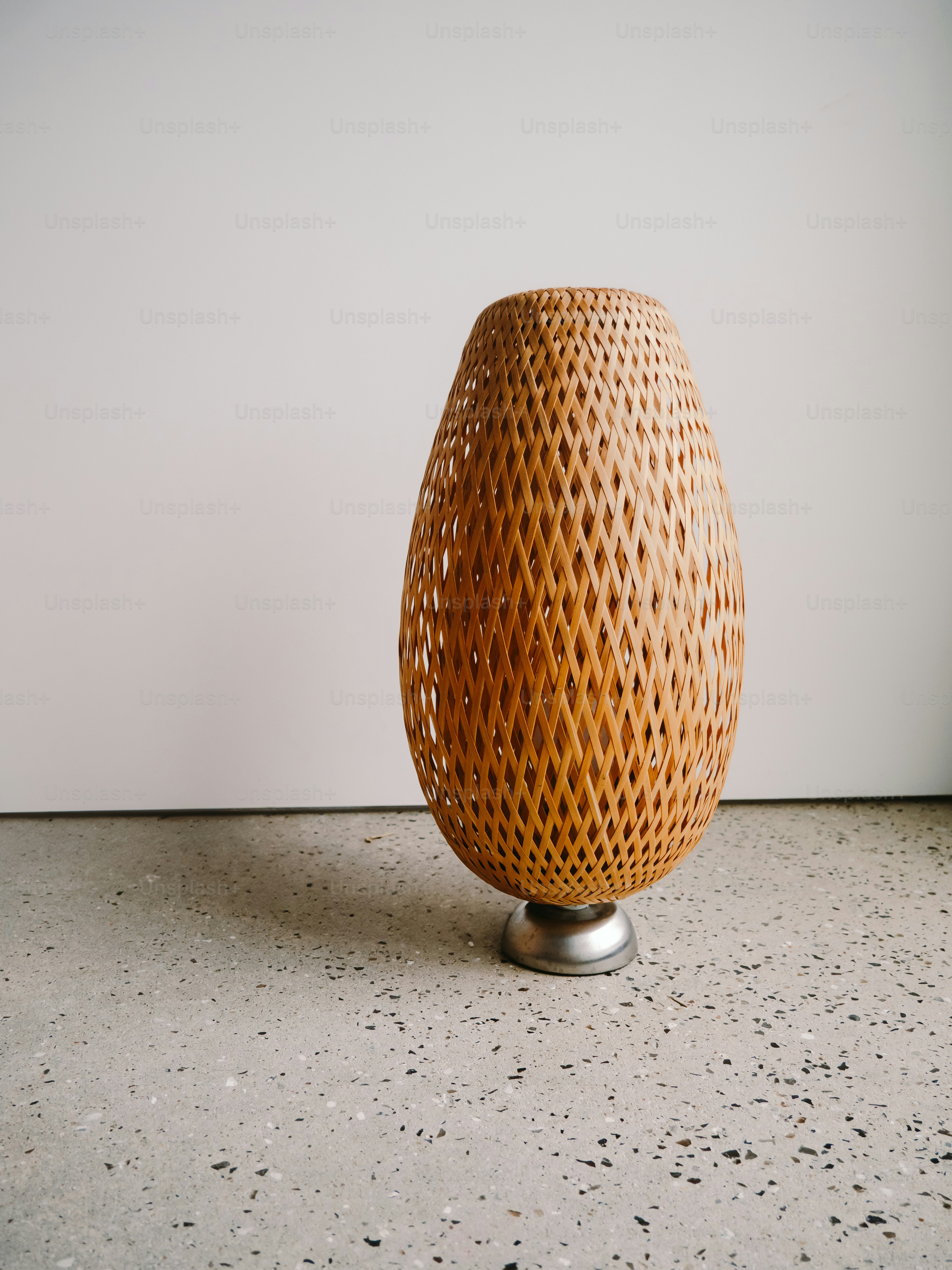 Lámpara de cesta tejida con base metálica sobre suelo de hormigón