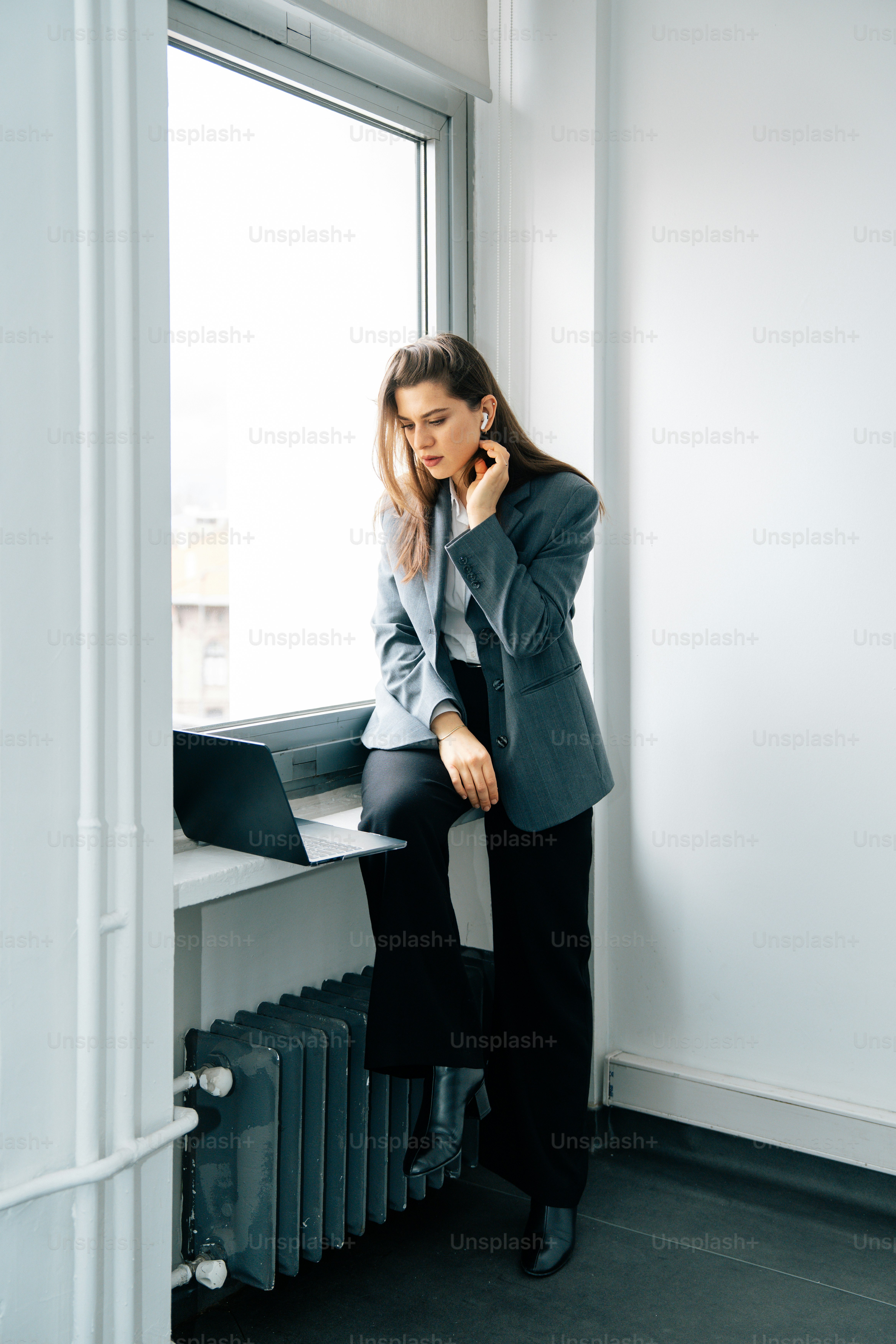 Woman in suit sitting by window with laptop