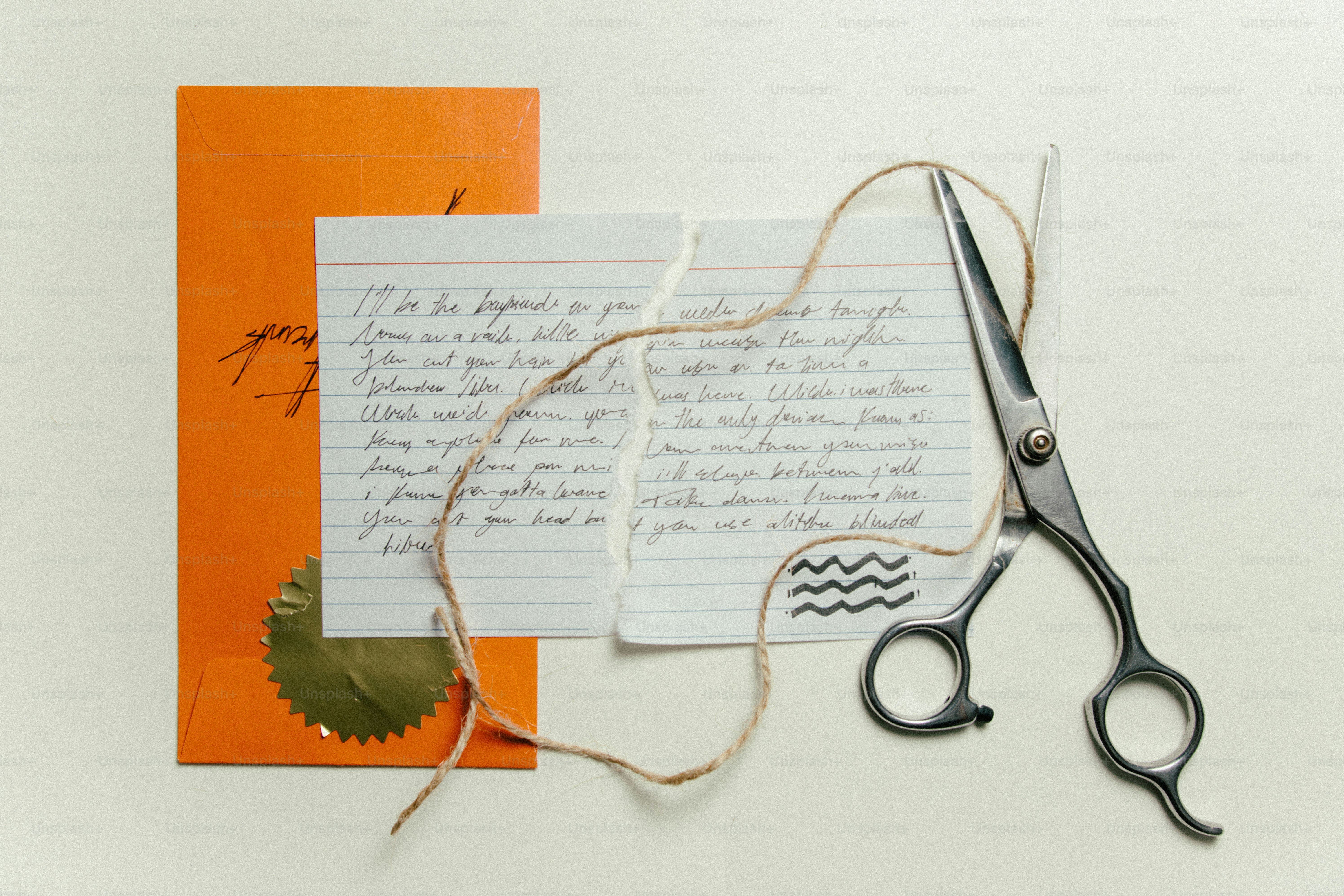 Scissors cutting a handwritten letter next to an orange envelope.