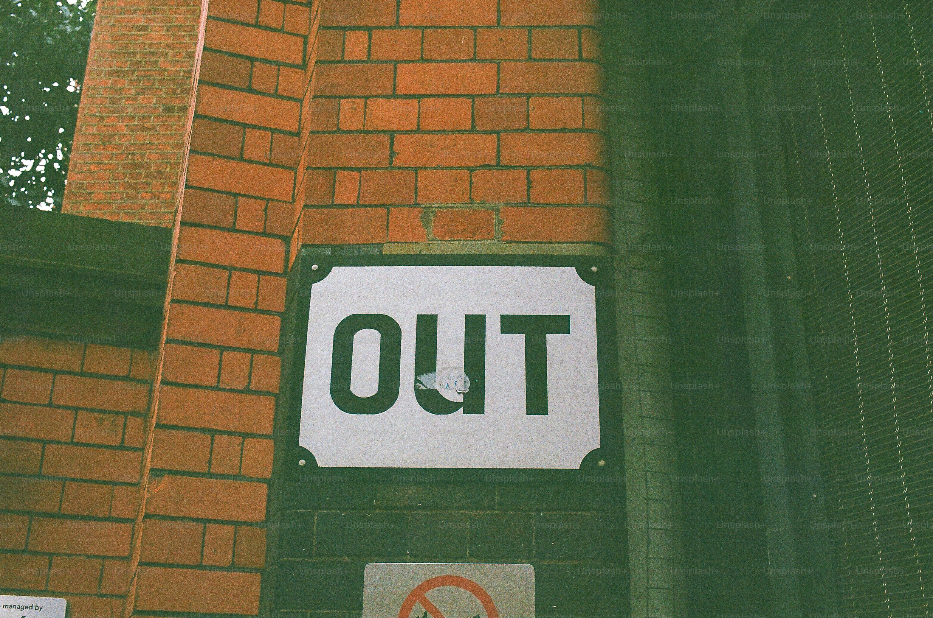 A white sign with the word out on brick wall.