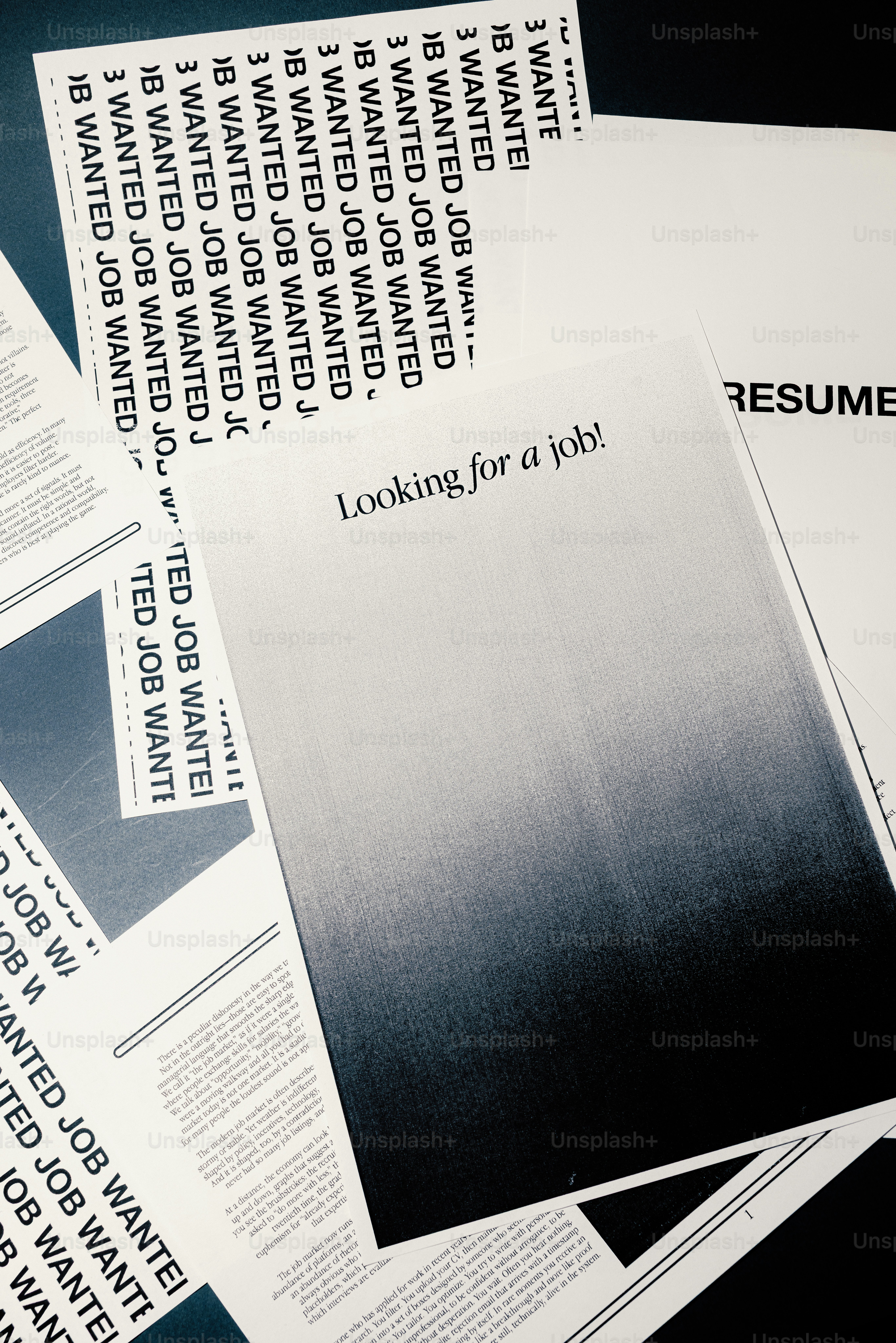 Job wanted flyers and resumes scattered on a dark surface.