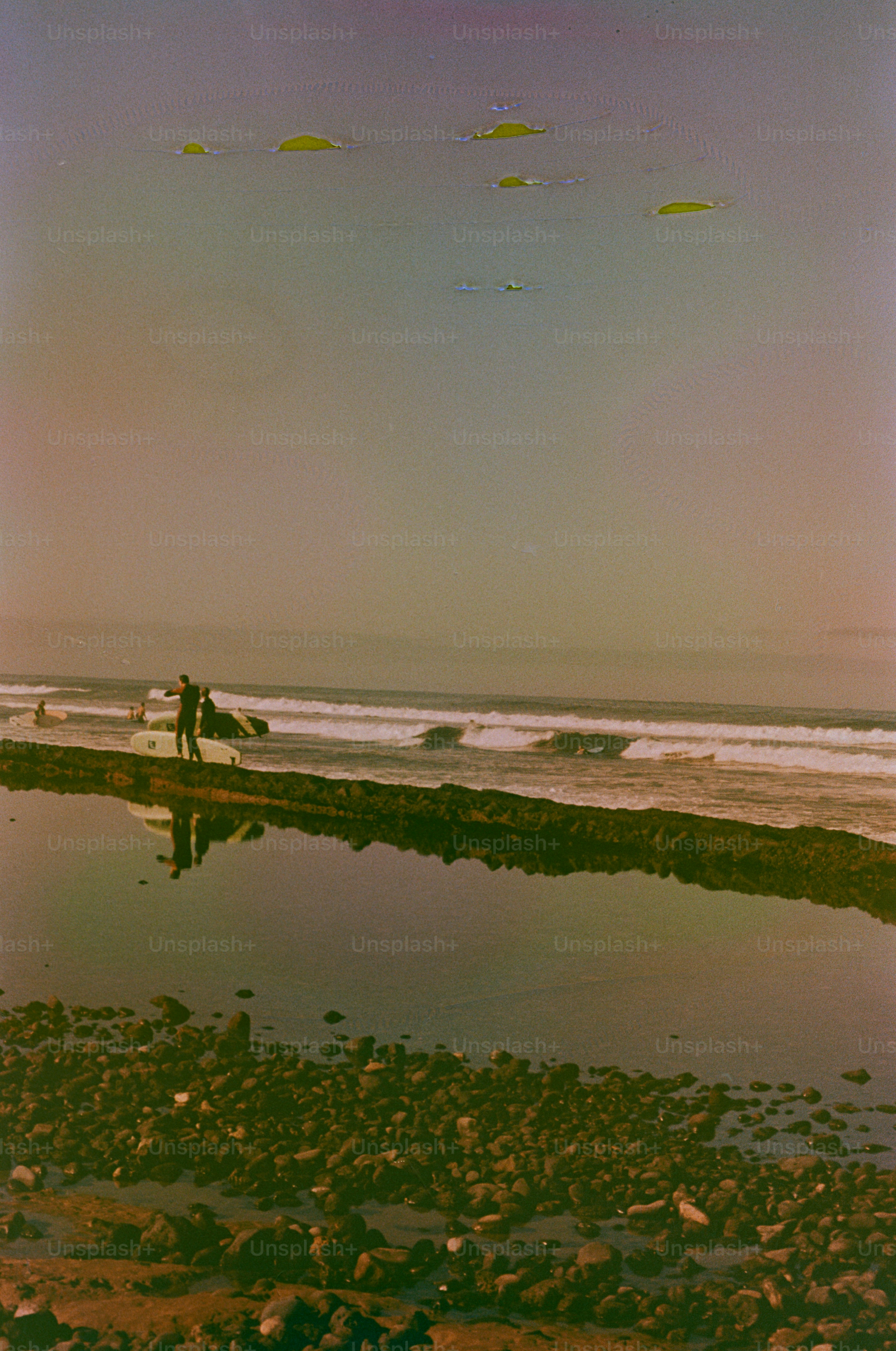 Surfers standing on a rocky shoreline with ocean waves