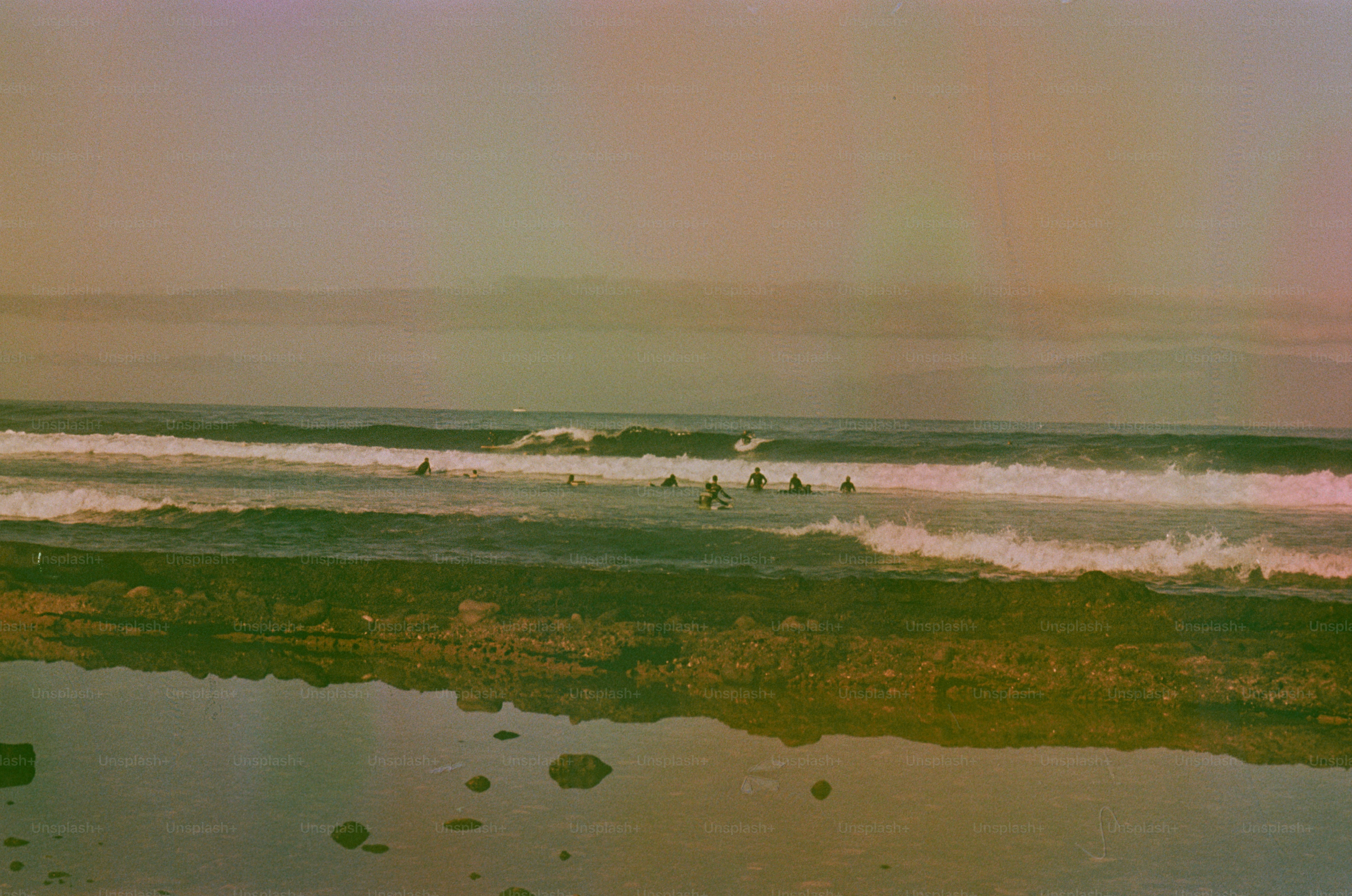 Surfers ride waves near a rocky shore.