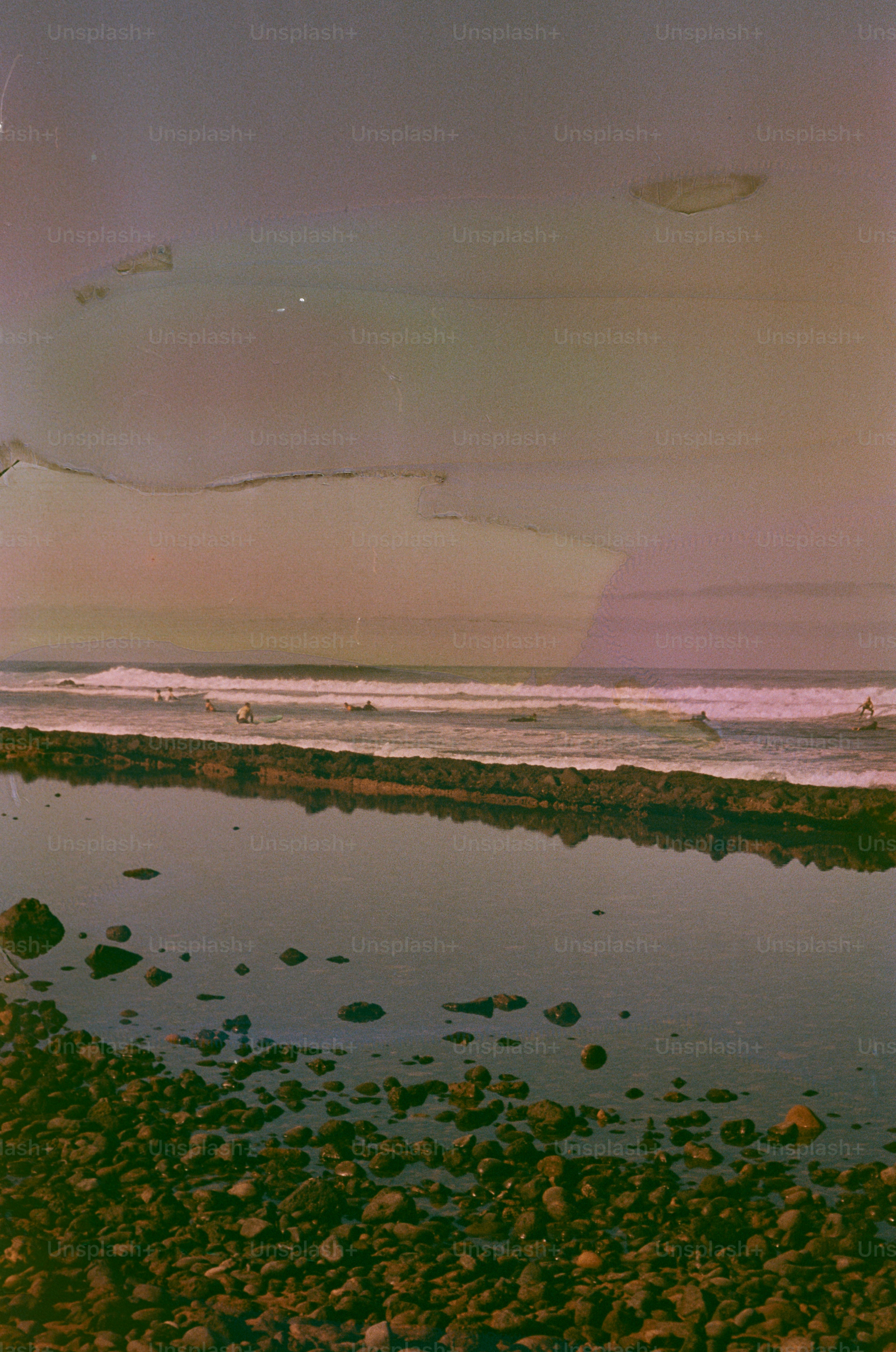 Surfers ride waves in a calm ocean with rocky shore.