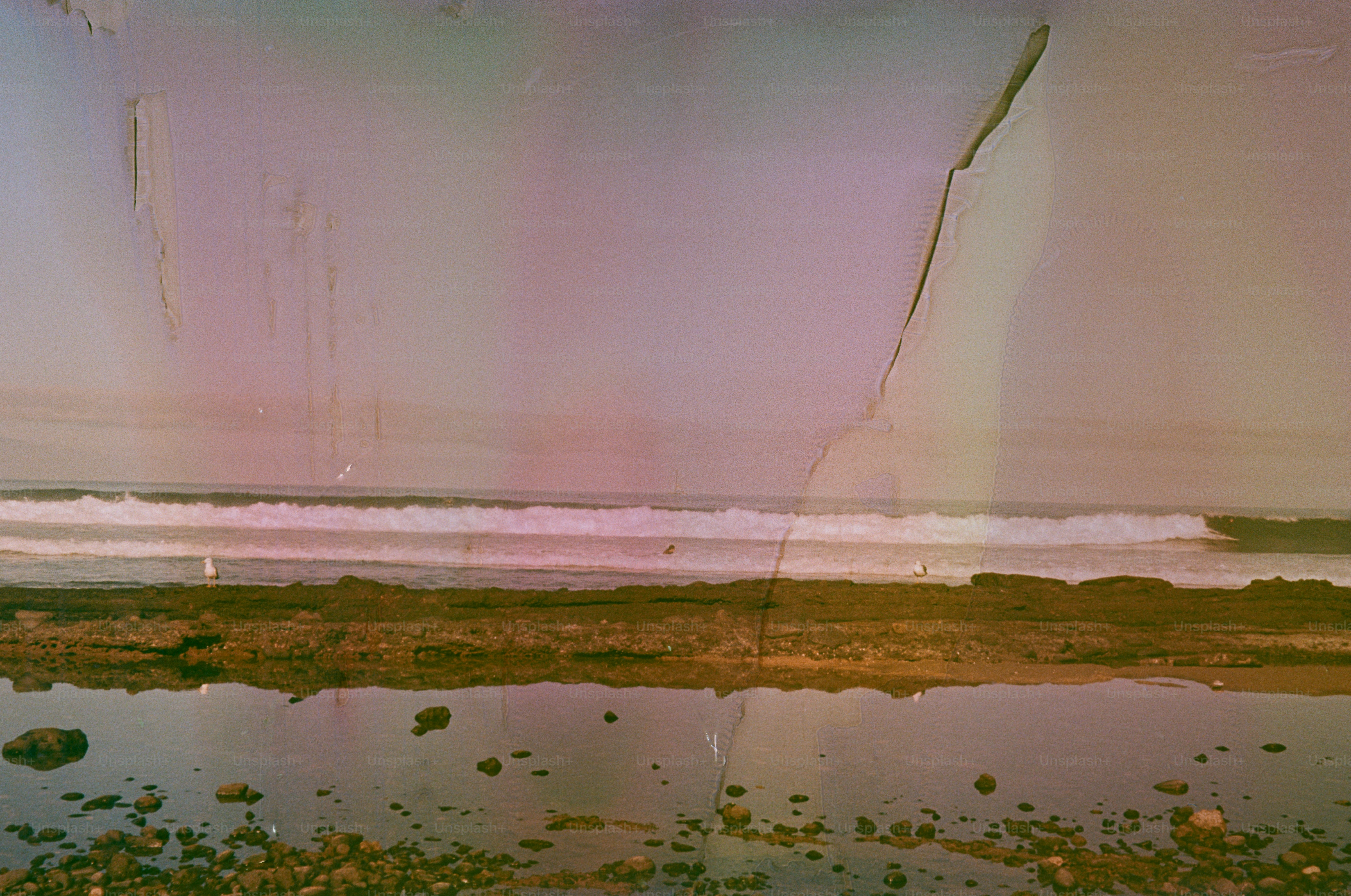 Waves crash on a rocky shore under a pastel sky