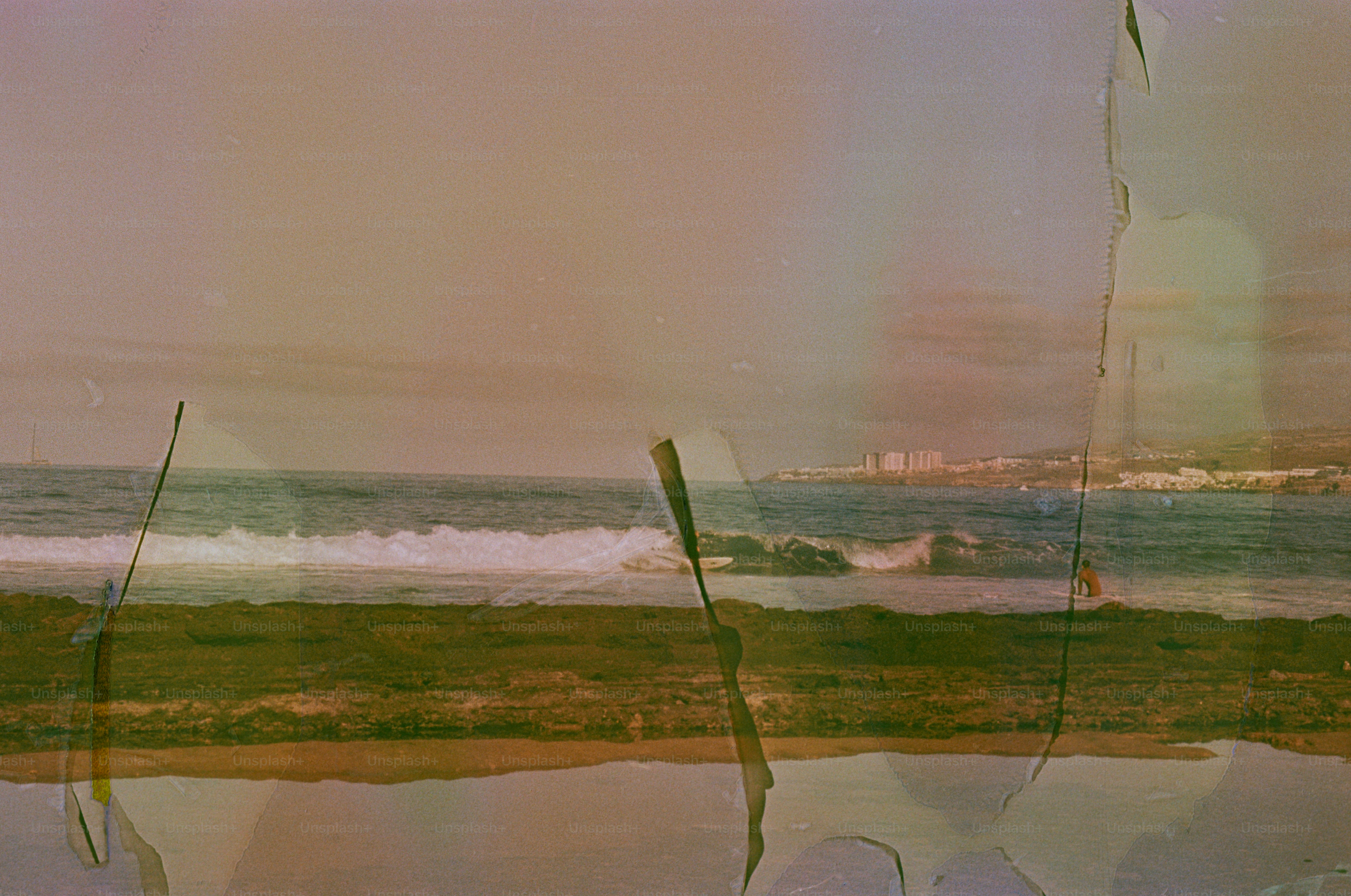 Ocean waves crash on a sandy beach with distant buildings.