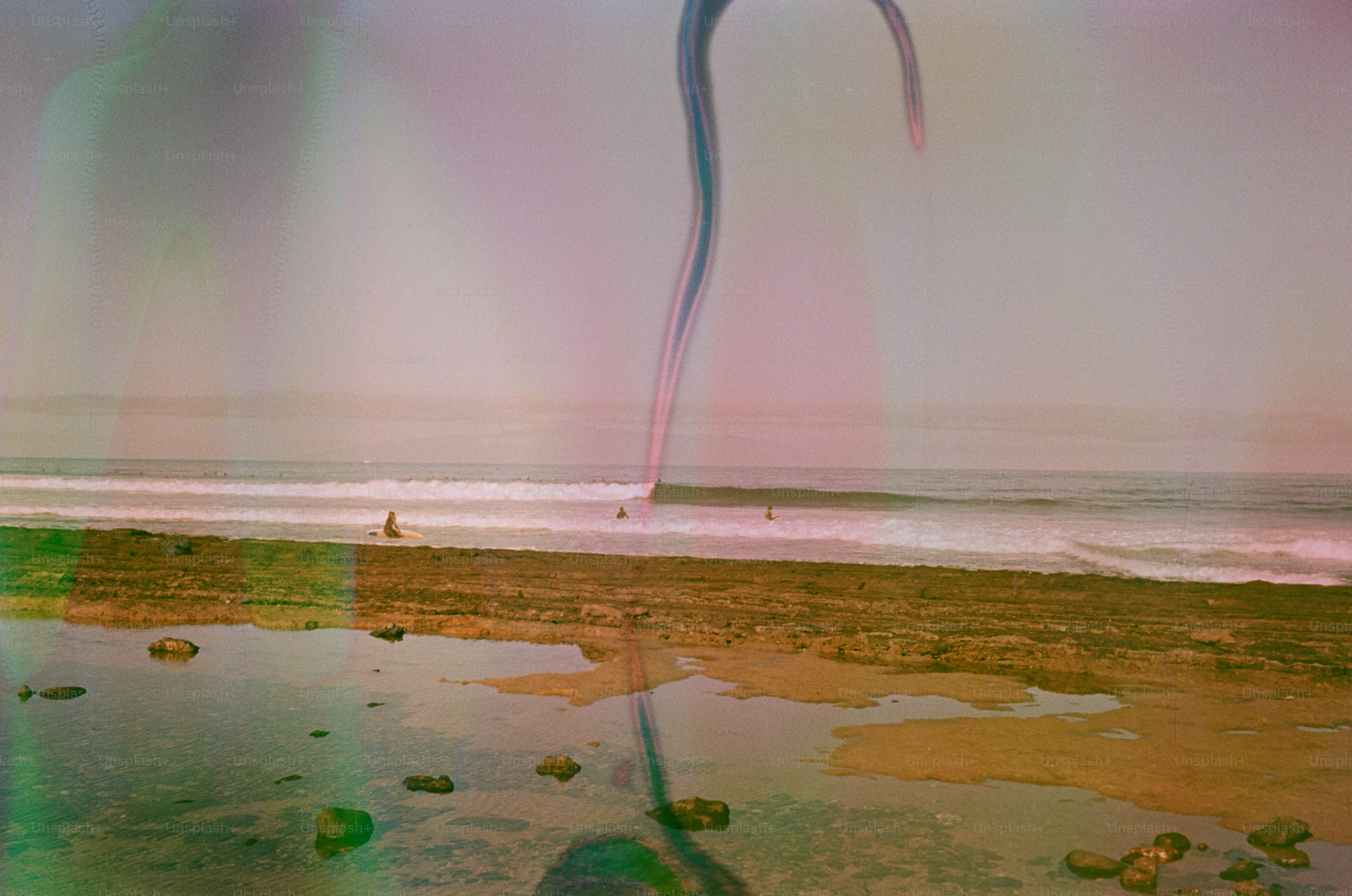 Surfers ride waves on a rocky beach at sunset.