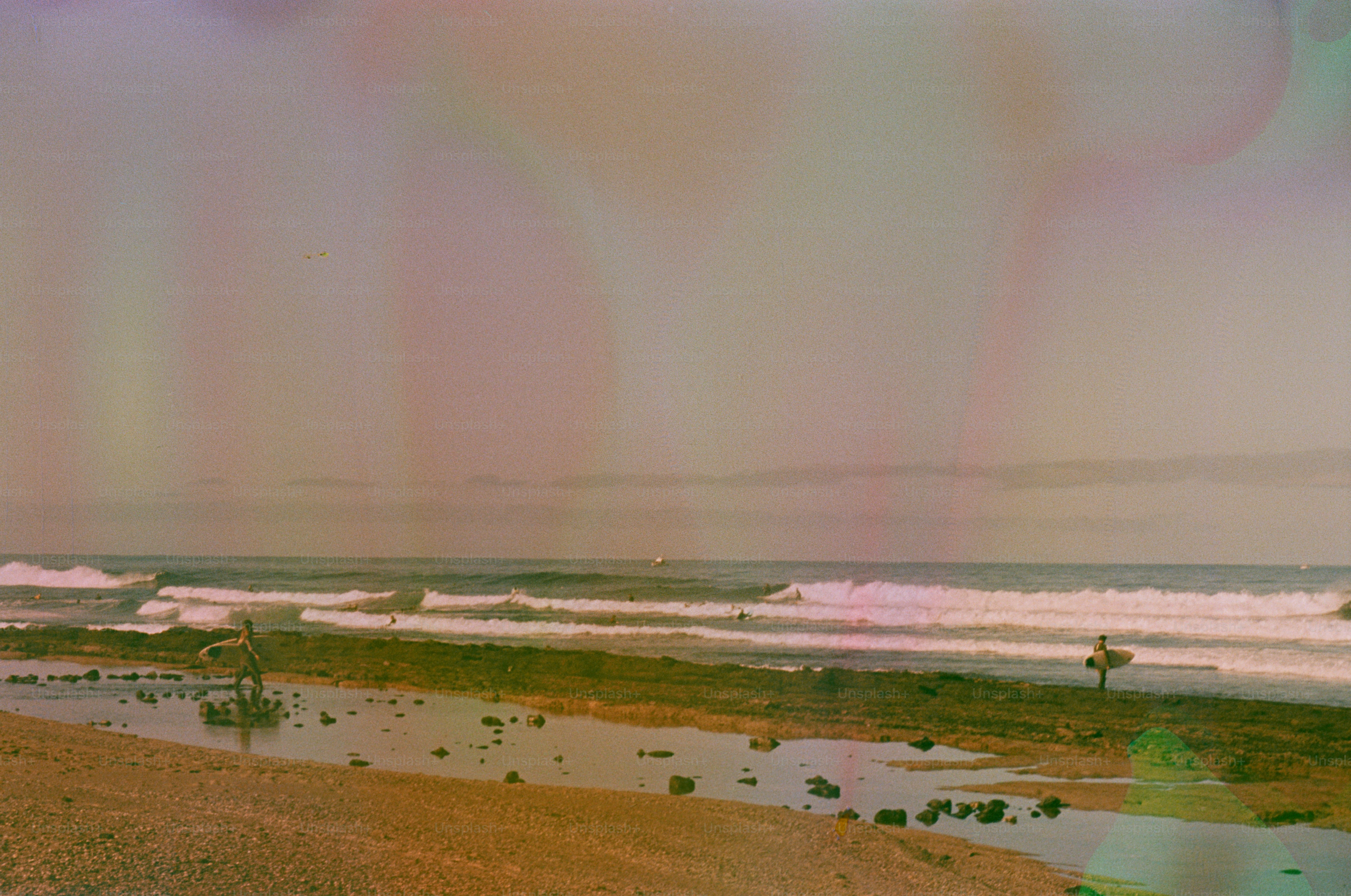 Surfers with surfboards on a beach at sunset
