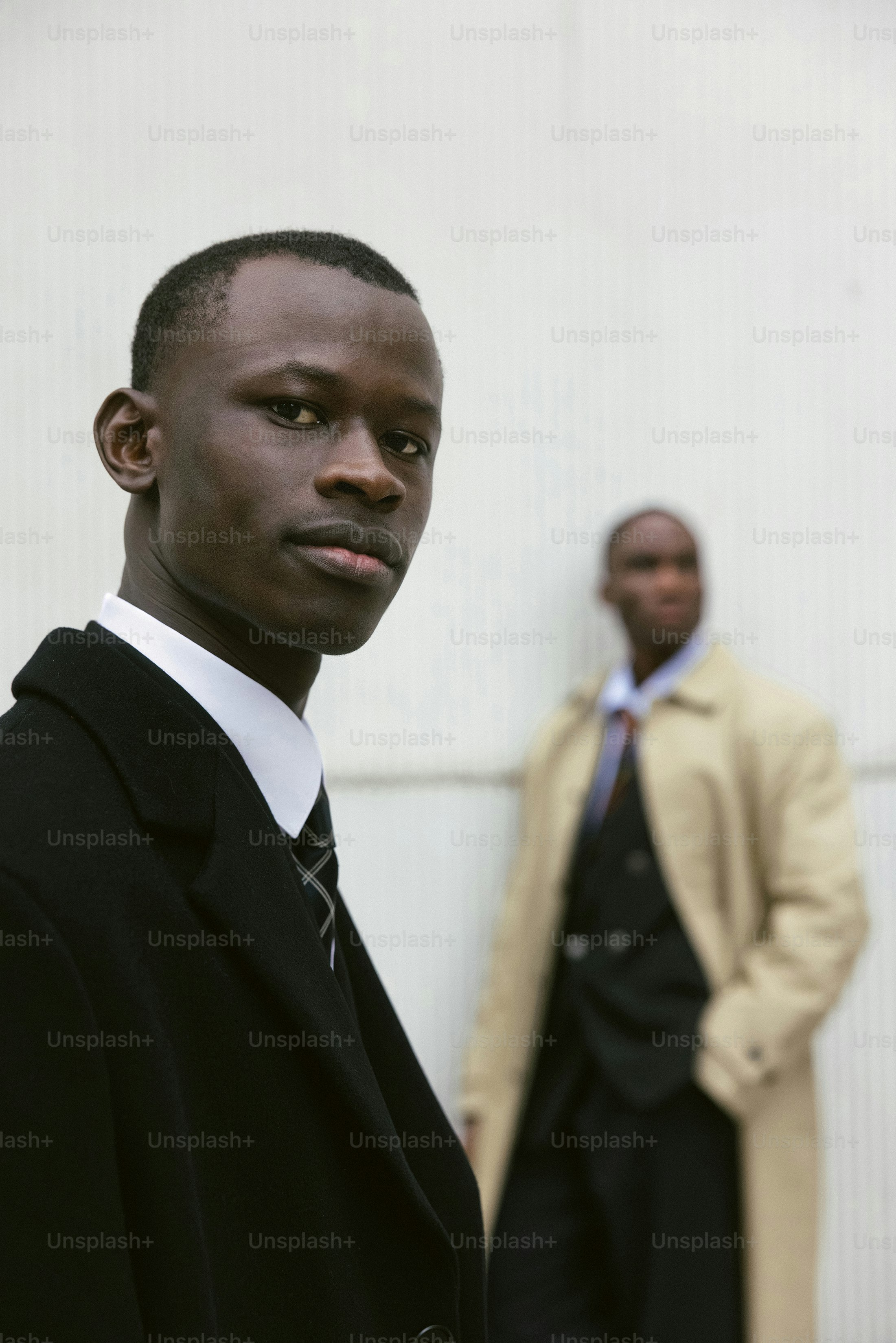 Two men in suits stand against a wall