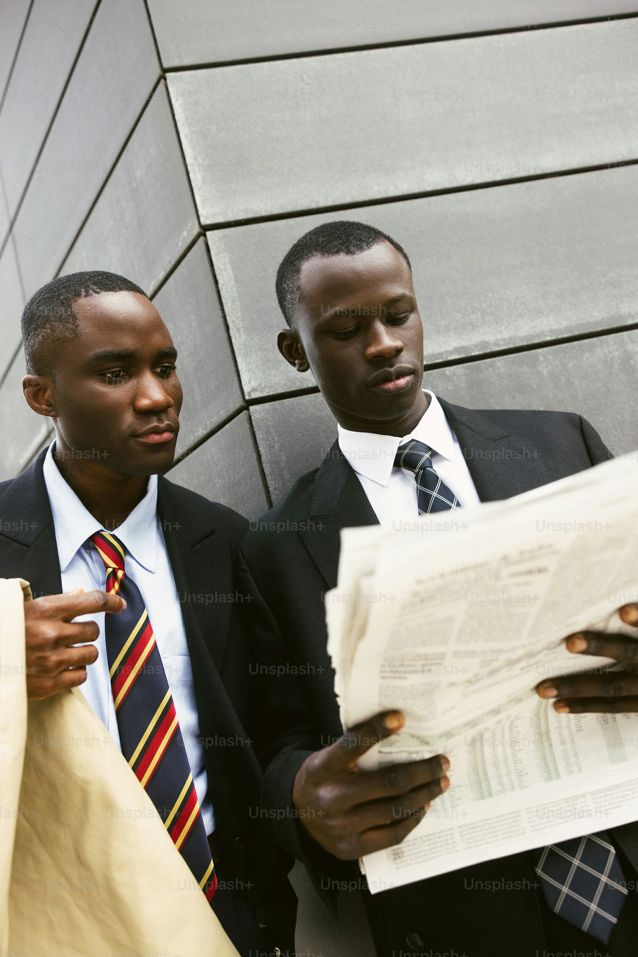 Two men in business attire reading a newspaper outside
