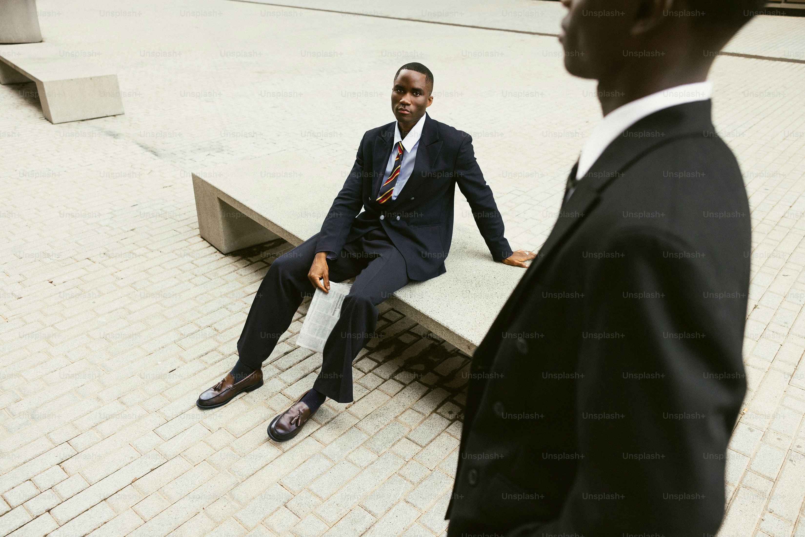 Two men in suits stand outside on a sidewalk.