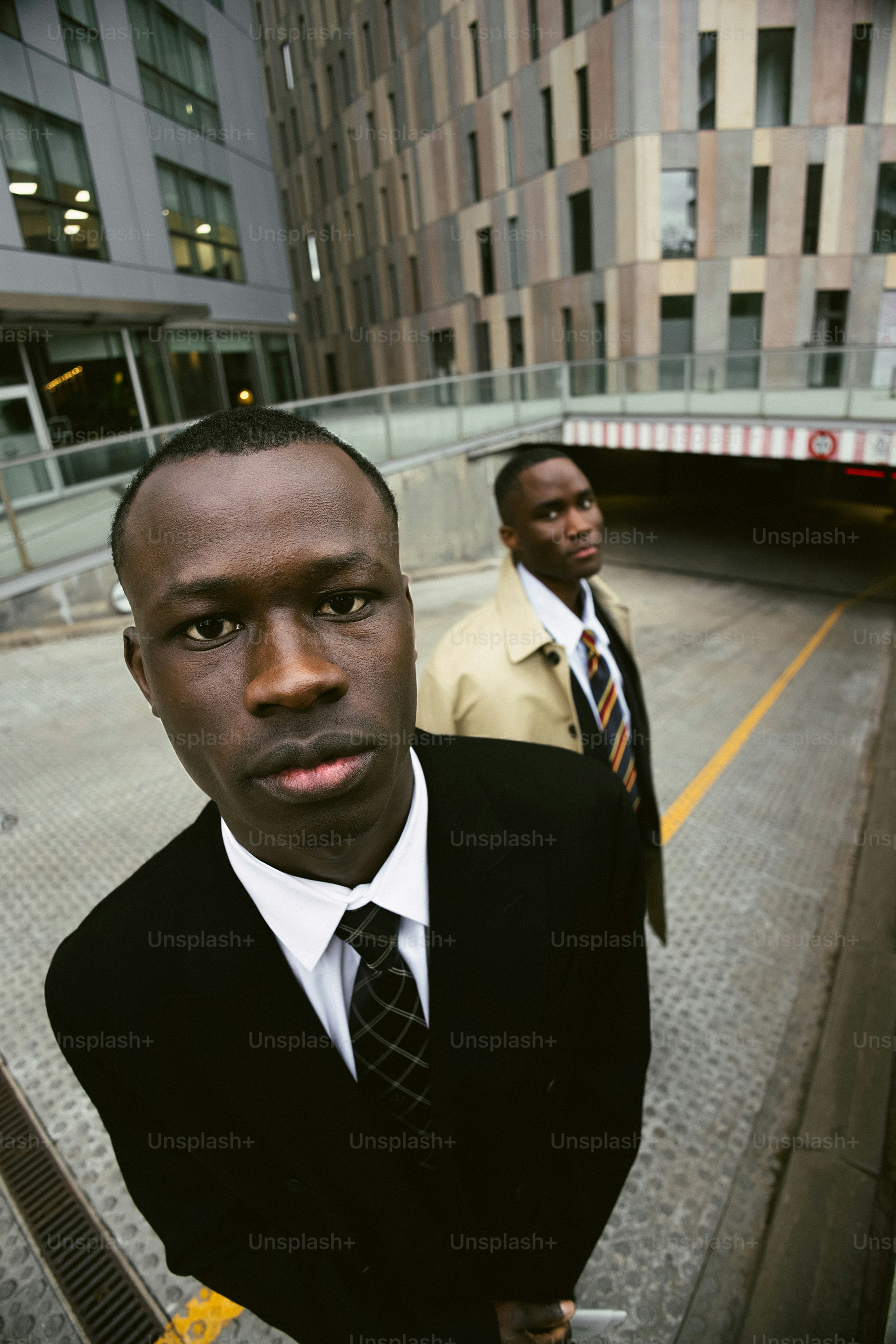Two men in suits stand outside modern buildings.