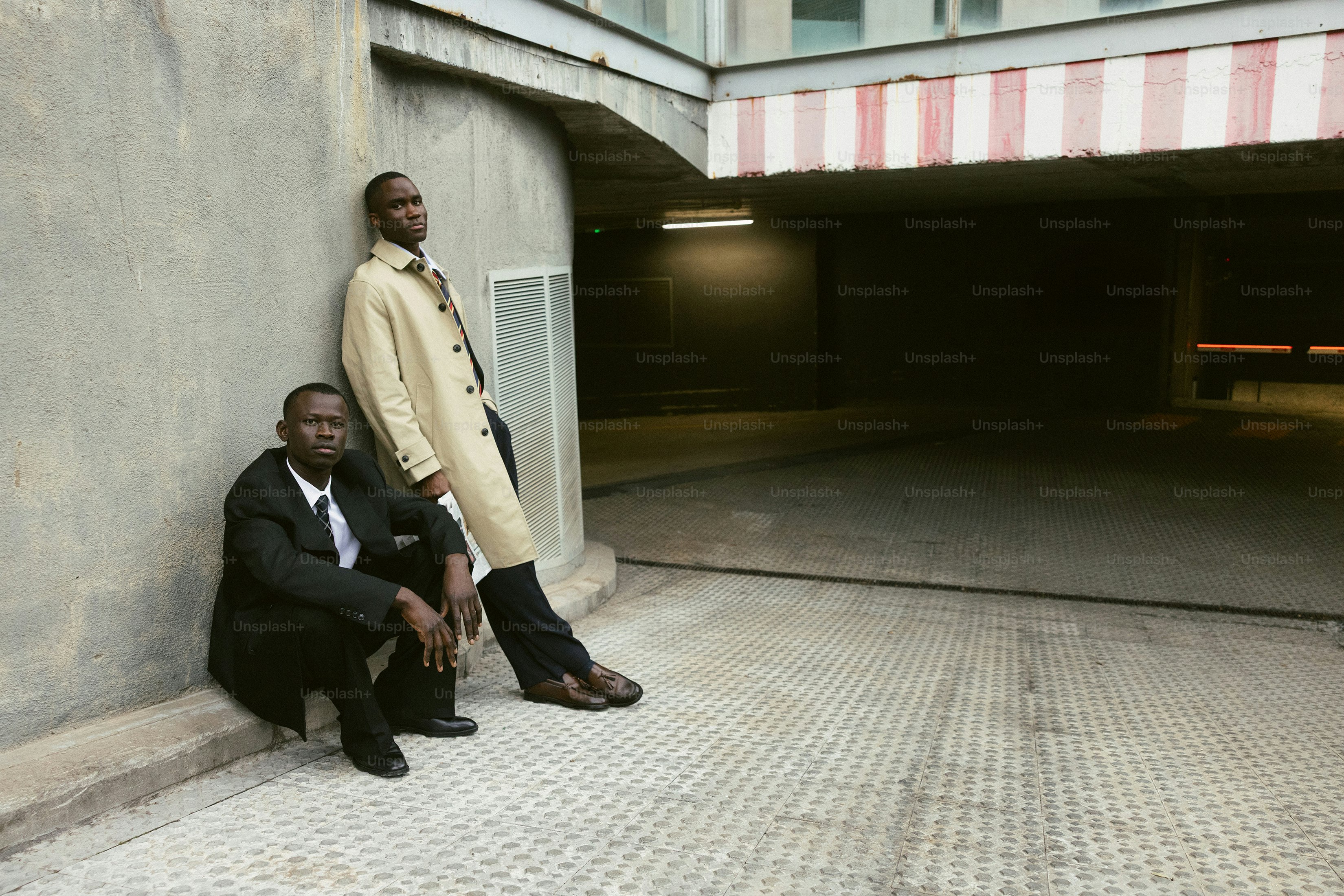 Two men in suits leaning against a wall.