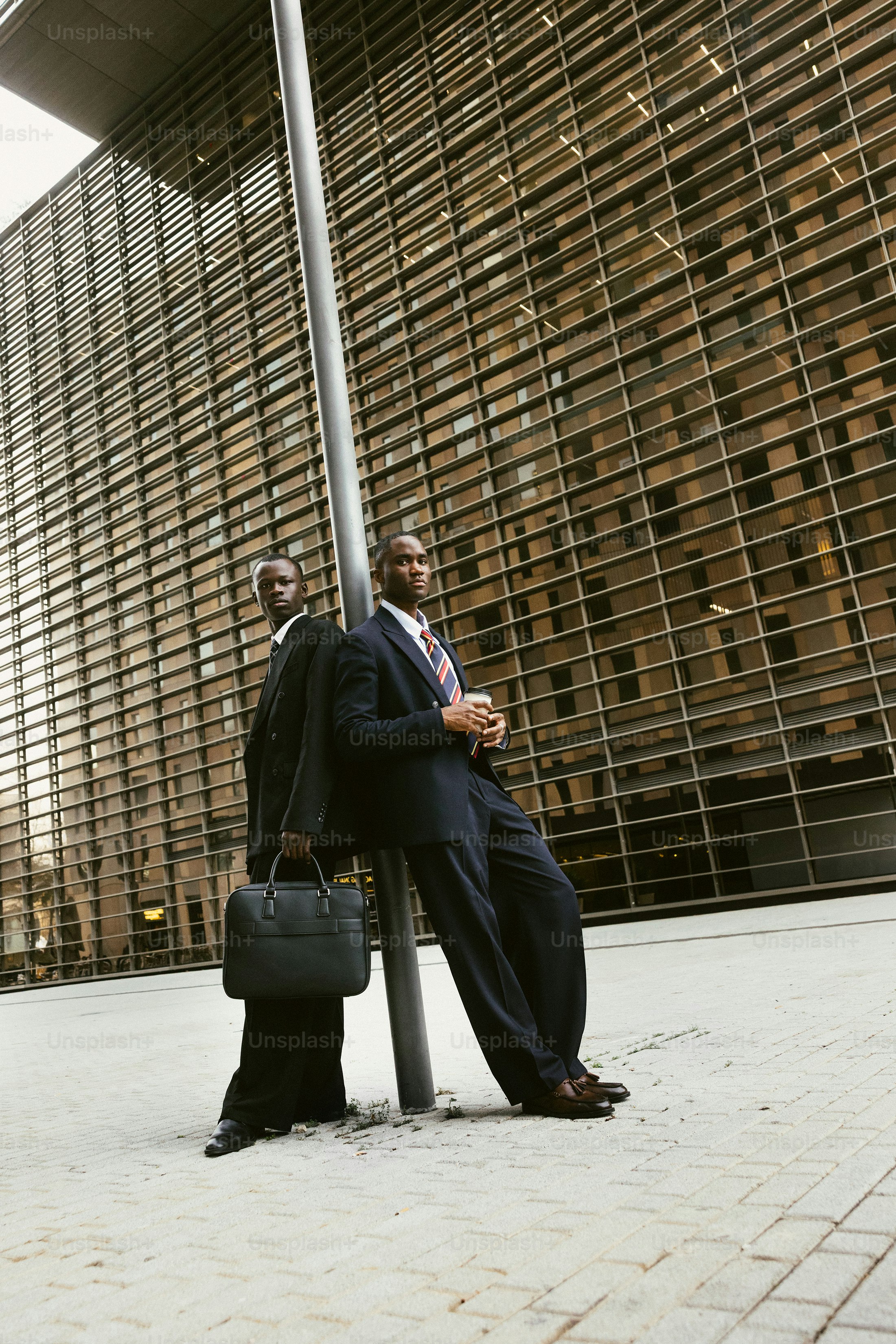 Two businessmen leaning against a pole outside building