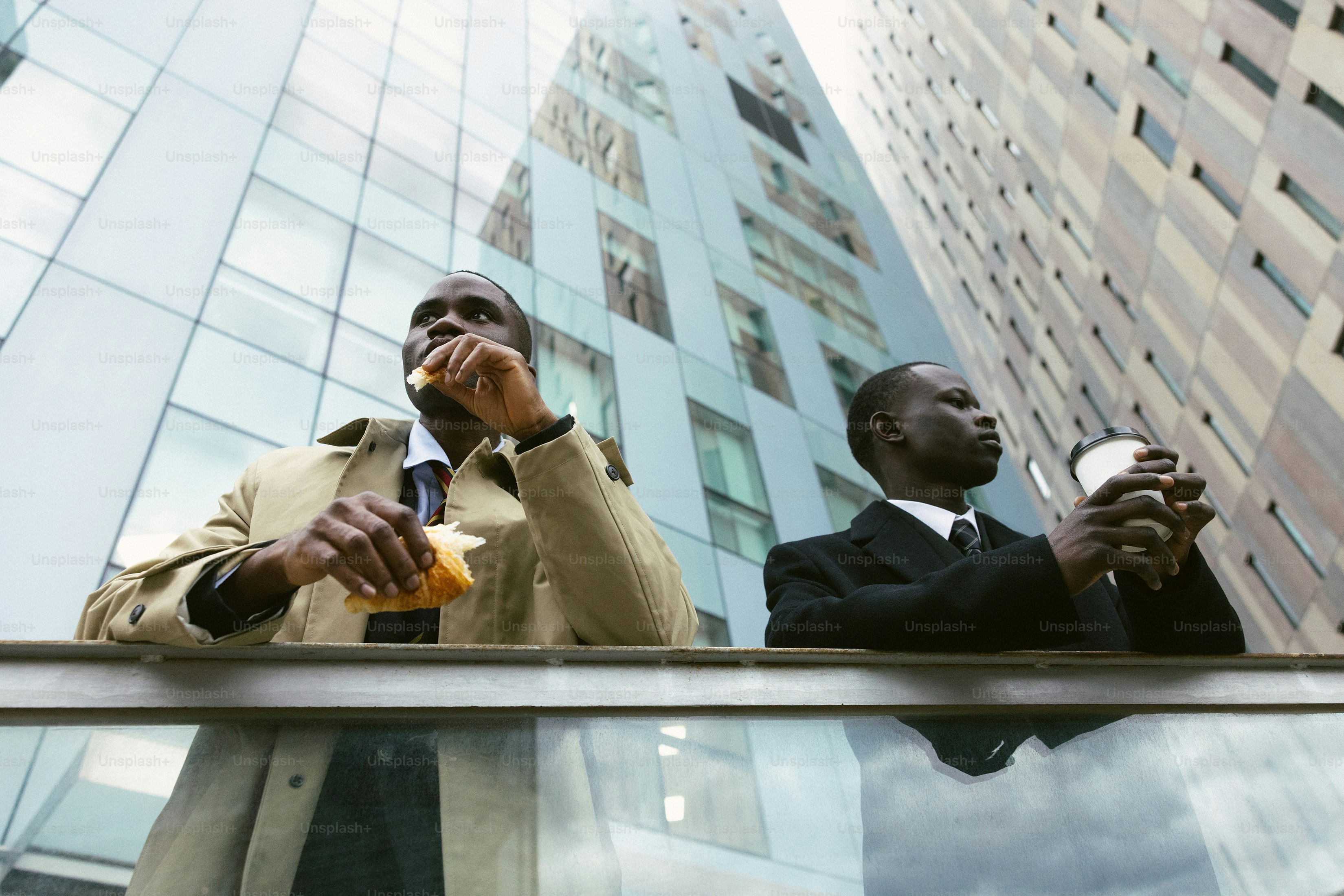 Two businessmen eating and drinking outside modern buildings