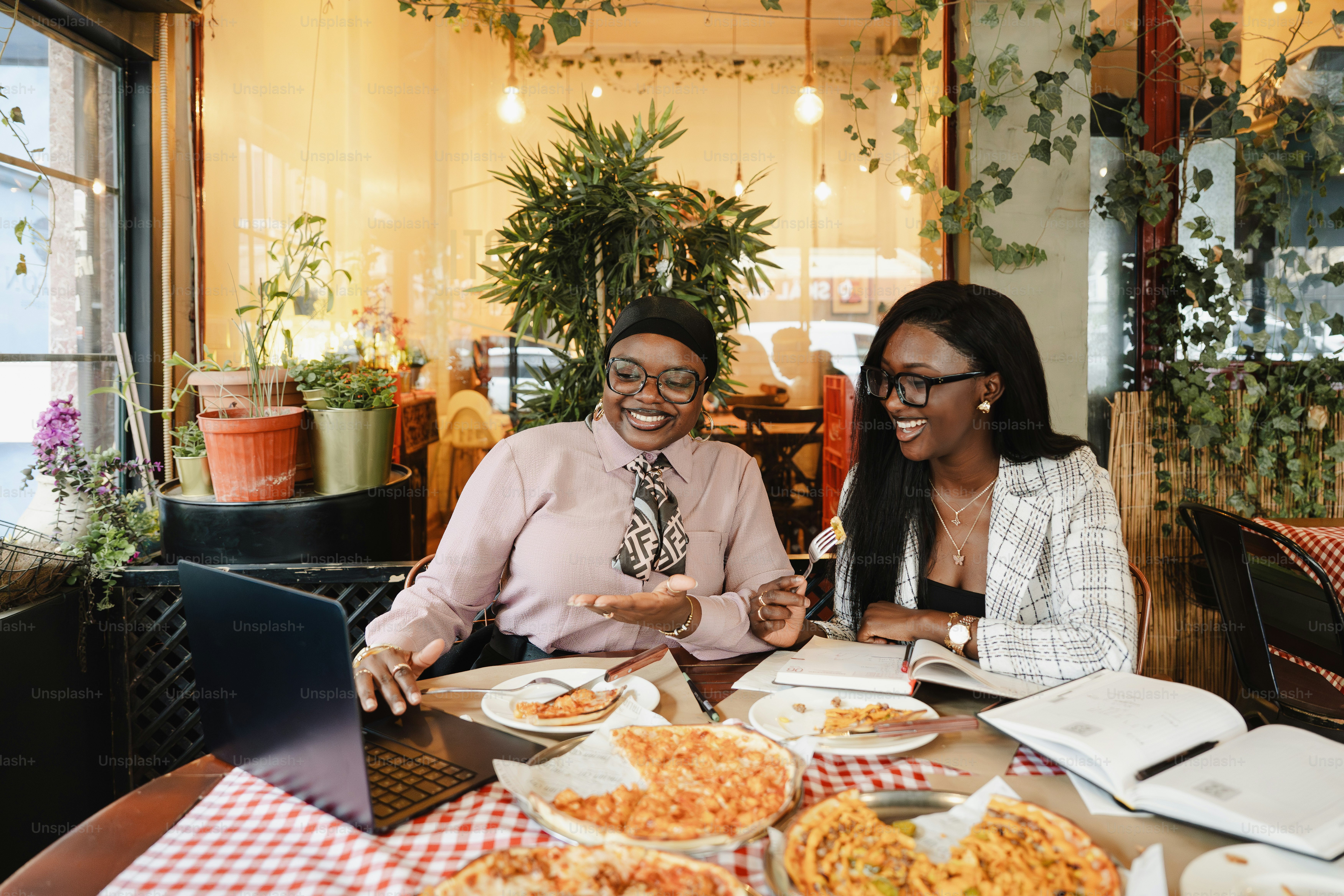 Duas mulheres rindo enquanto trabalham em um café com pizza.