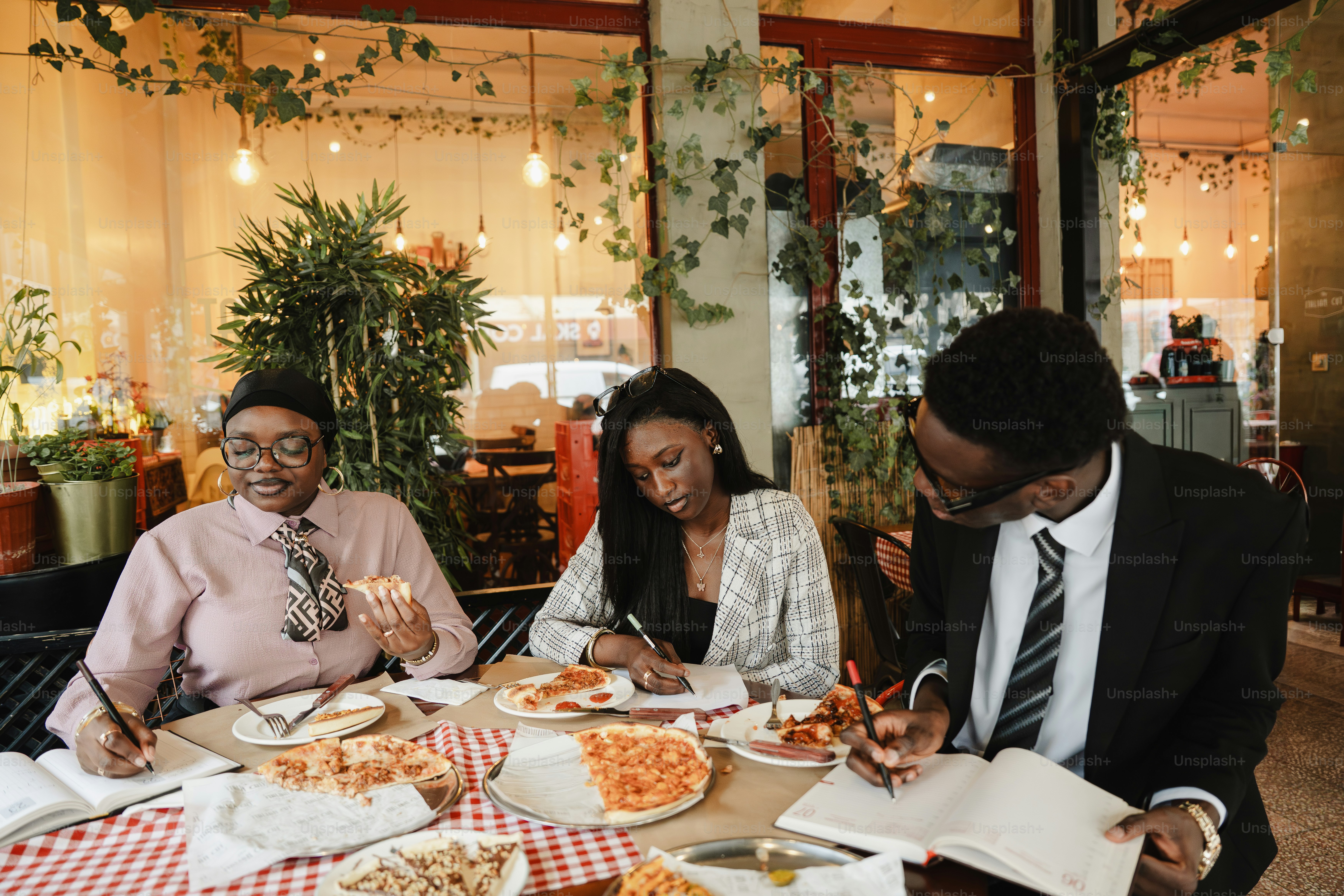 Três pessoas estudando juntas numa mesa com pizza.