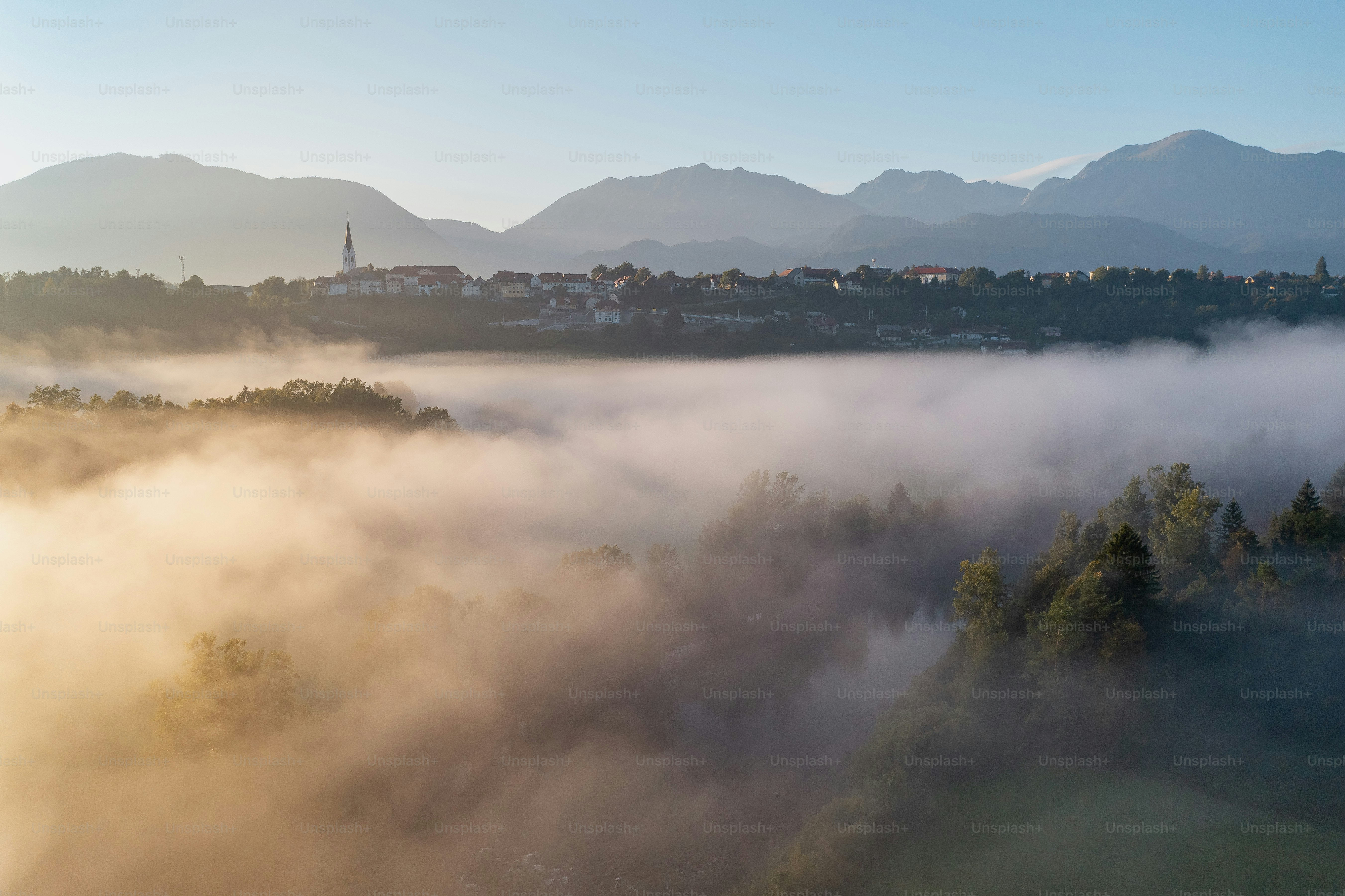 Neblige Morgenlandschaft mit fernen Bergen und einem Dorf.